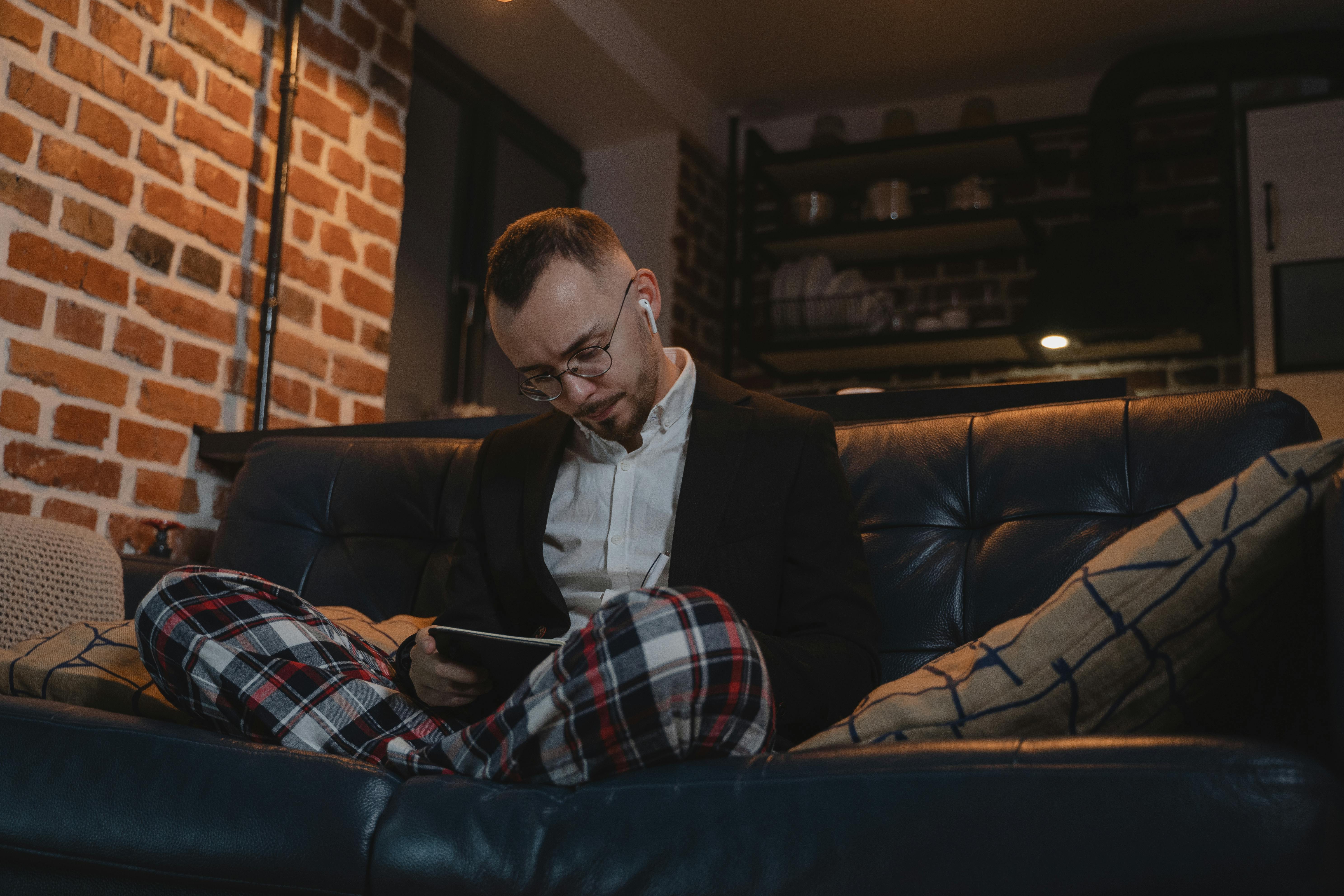 Un homme habillé d'un pantalon de pyjama et d'une veste assis sur un canapé | Source : Pexels