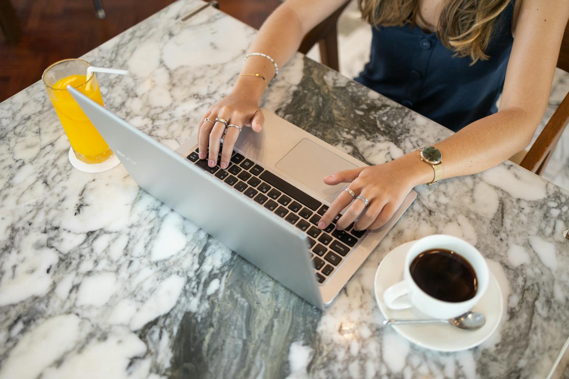 Une femme travaillant sur son ordinateur portable avec une tasse de café et un jus de fruit posés sur la table devant elle | Source : Pexels