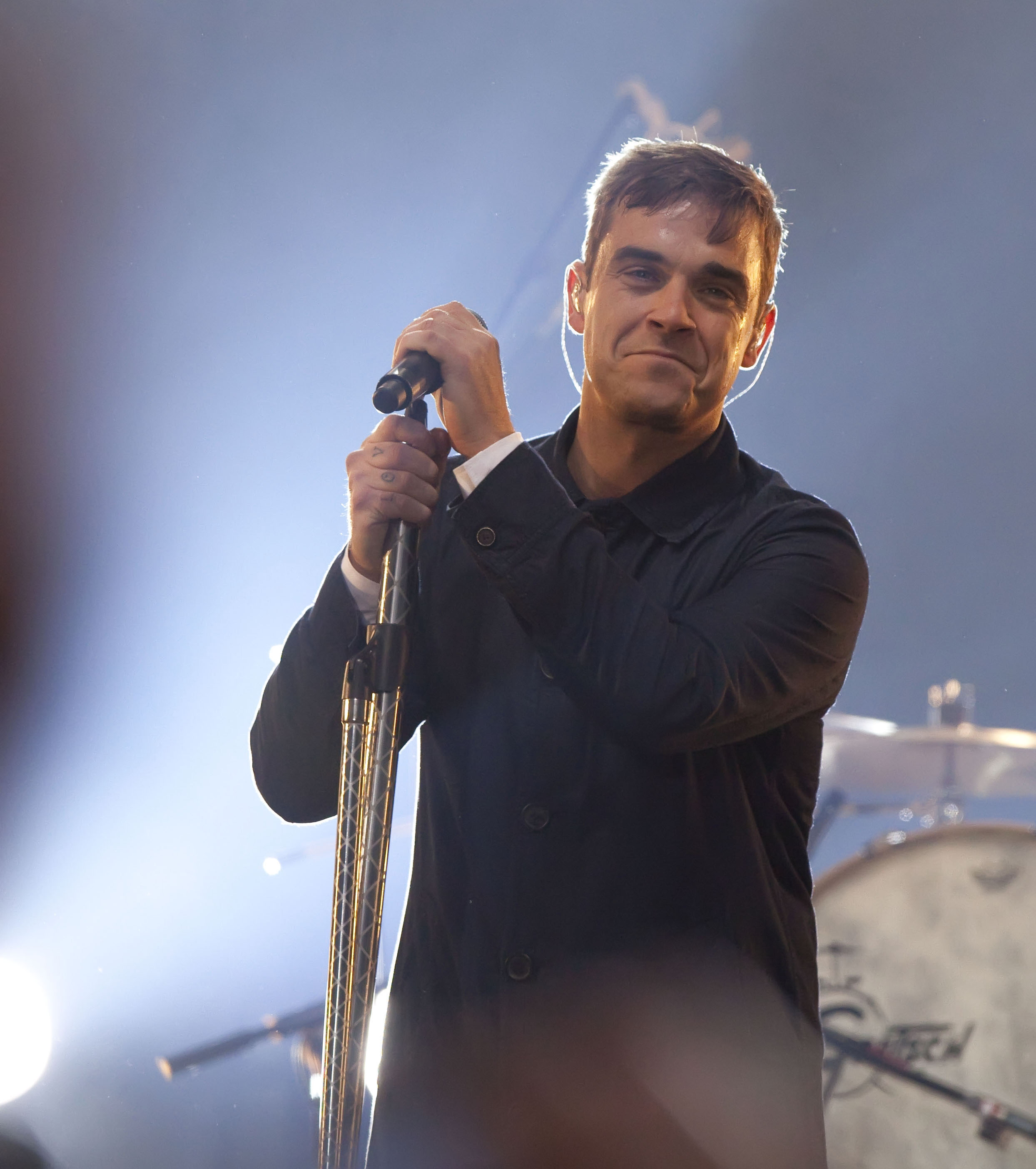 Robbie Williams se produit en concert lors d'un concert pop-up gratuit à Berlin, en Allemagne, le 23 octobre 2009. Saisissant le pied du micro avec un sourire, il offre un spectacle intimiste qui permet aux fans de découvrir le charisme débordant d'énergie qui caractérise ses performances live.