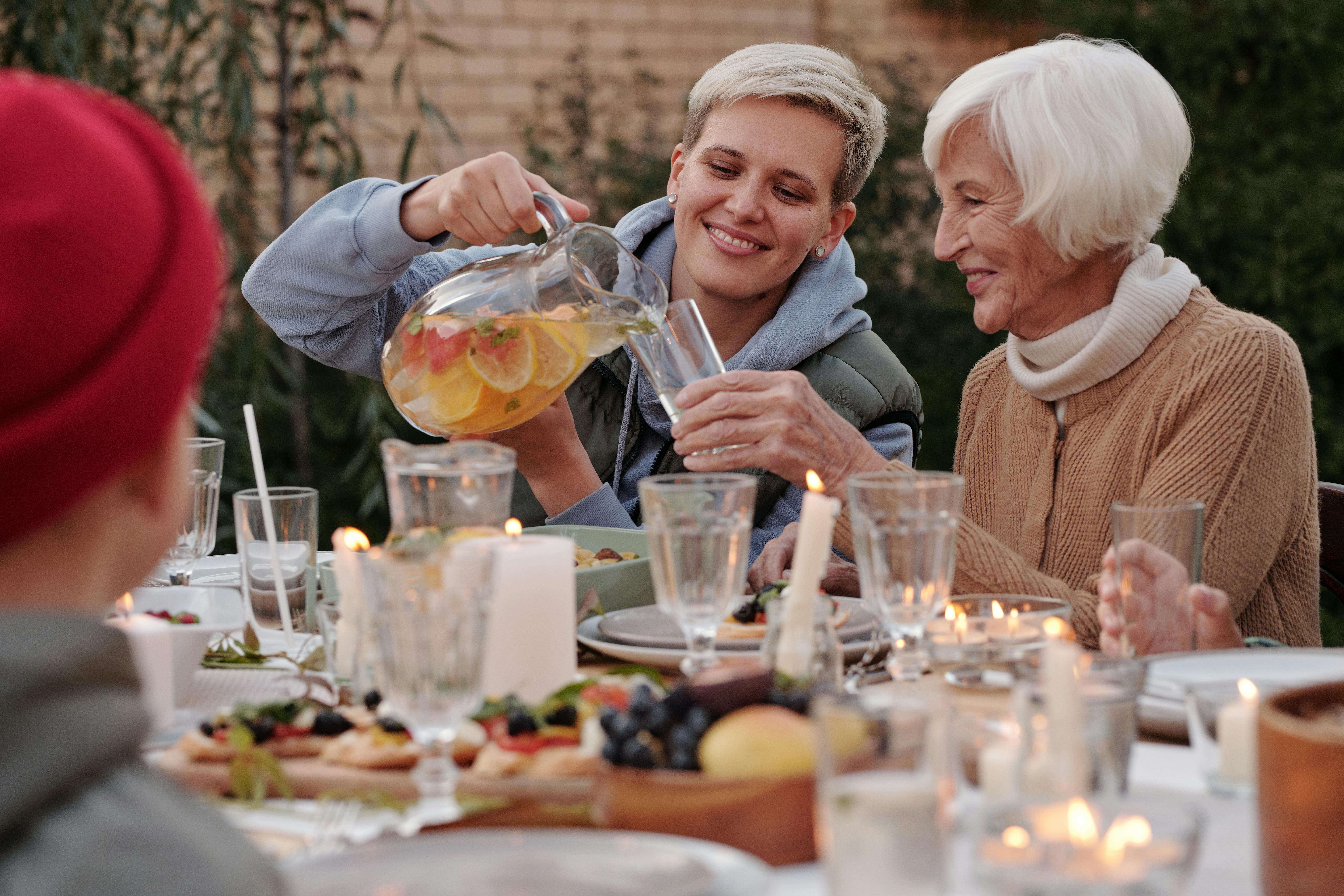 Une jeune femme joyeuse remplit le verre d'une femme plus âgée avec du punch alors qu'elles sourient toutes les deux I Source : Pexels