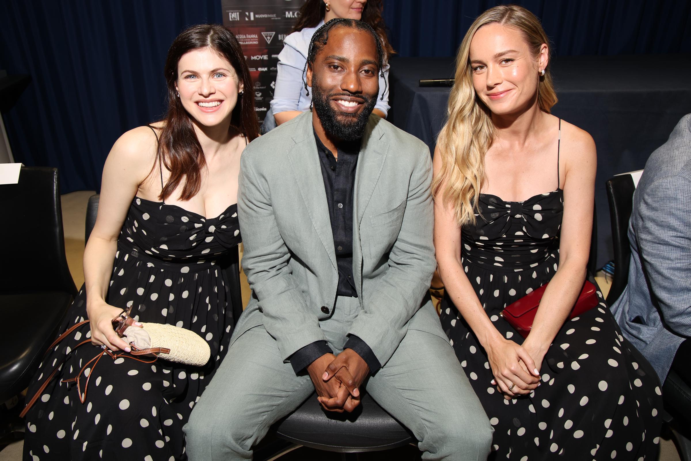 Alexandra Daddario et Brie Larson posent avec John David Washington entre elles lors de la conférence de presse Filming Italy, le 20 juin 2024, à Cagliari, en Italie. Les deux actrices portent la même robe à pois noire et blanche Dôen « Maryanna », créant ainsi un moment chic et harmonieux.