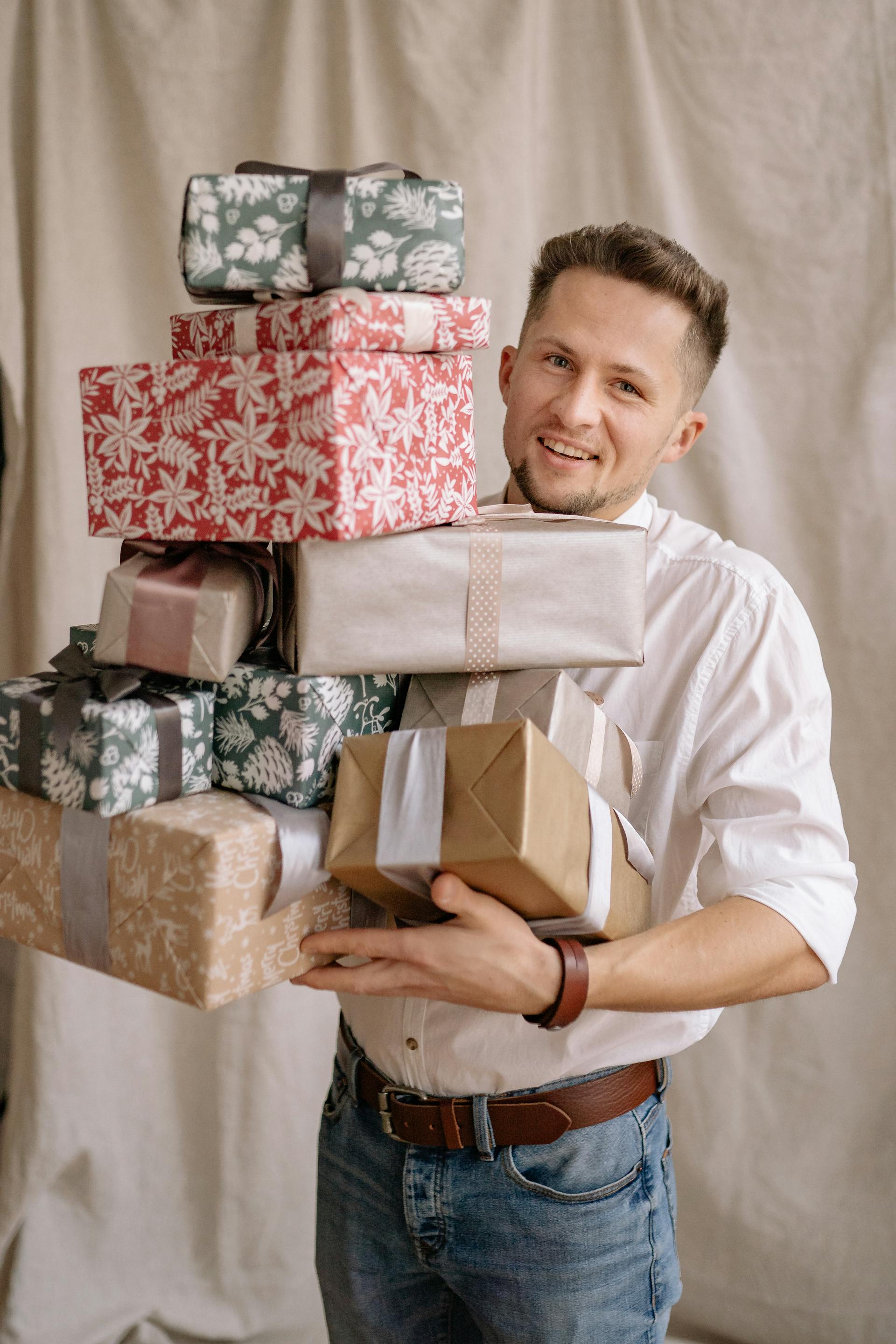 Un homme en chemise blanche et en jean tenant une grande pile de cadeaux emballés | Source : Pexels