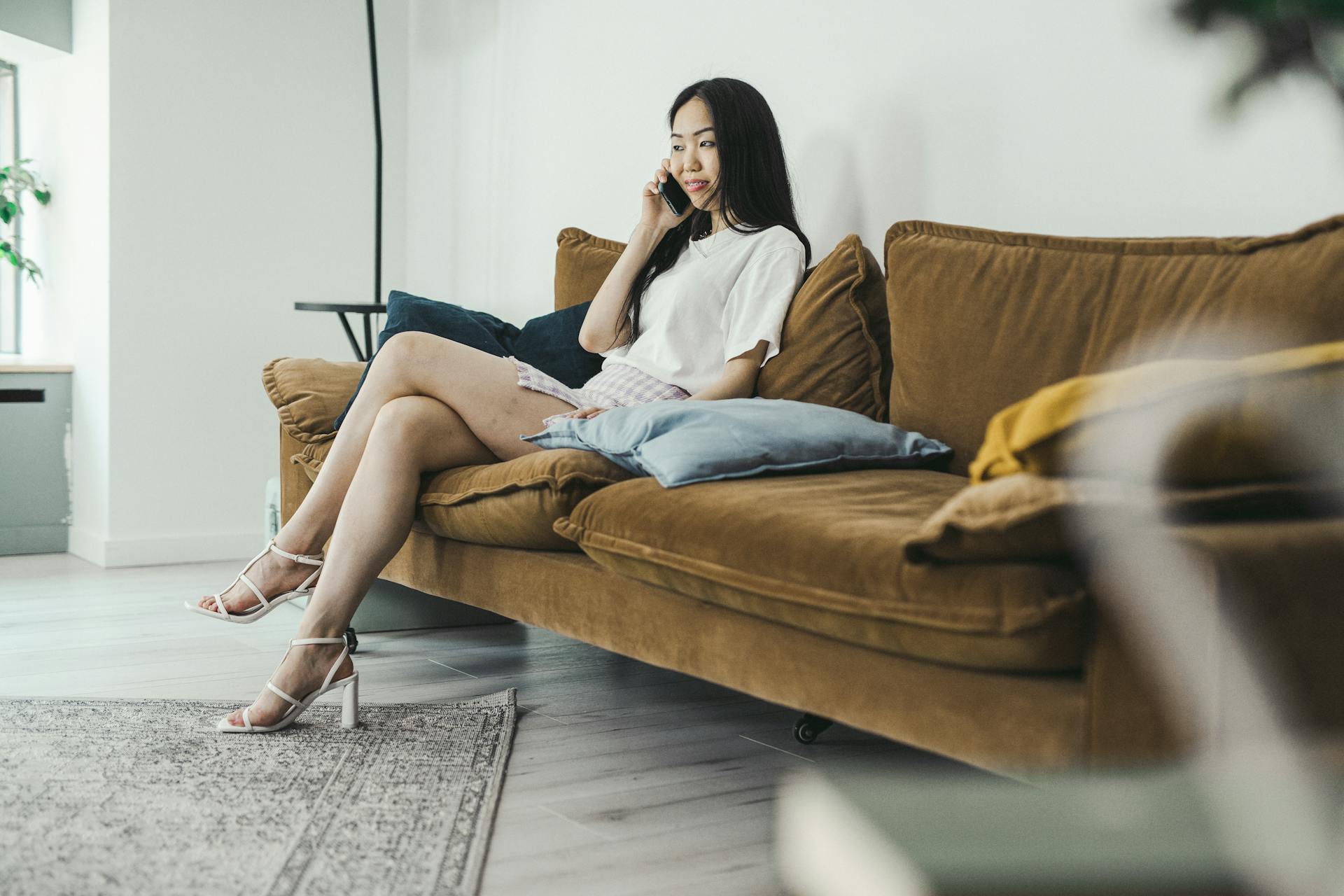 Une jeune femme en talons hauts assise sur un canapé marron en train de parler au téléphone | Source : Pexels