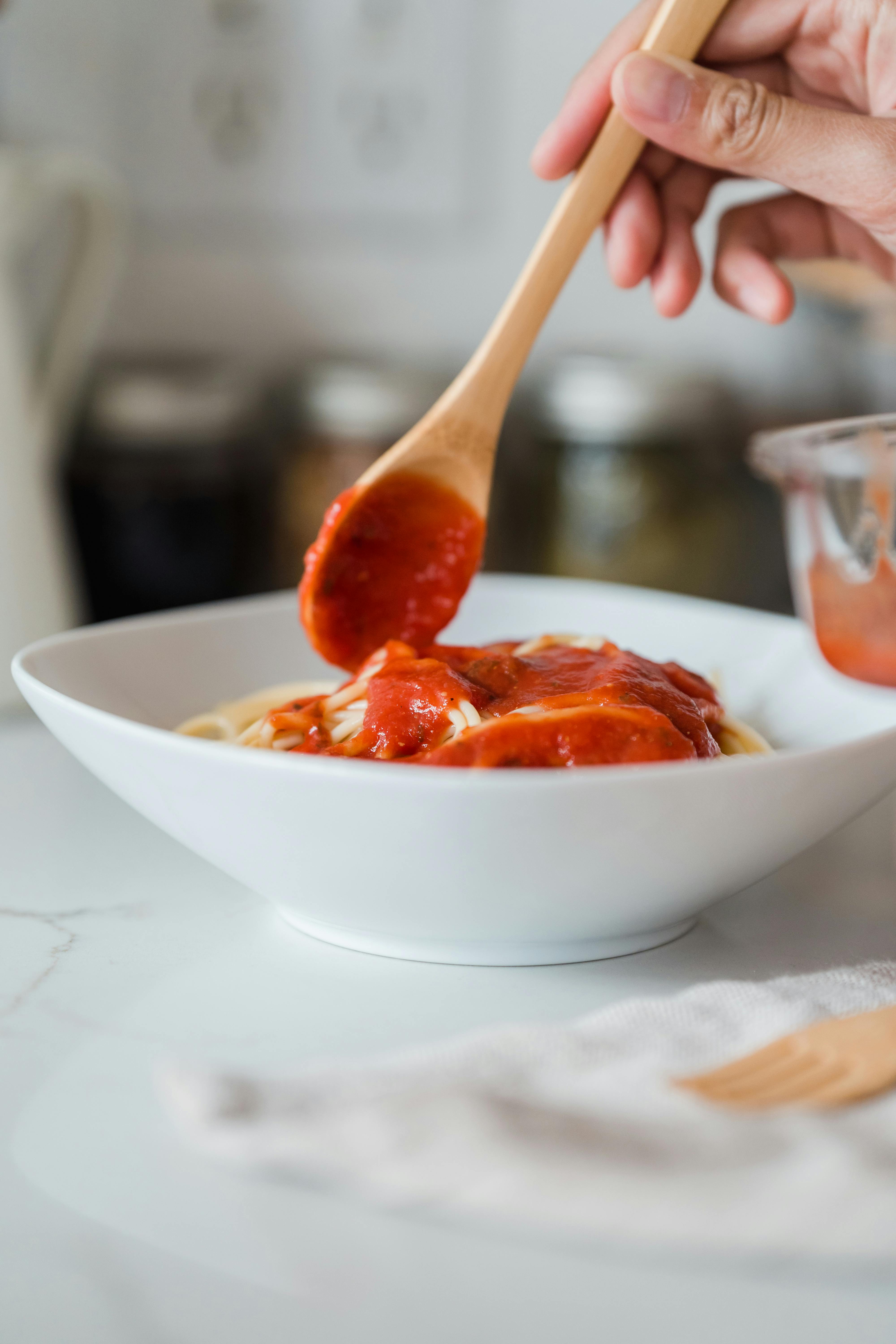 Une personne ajoutant de la sauce aux pâtes | Source : Pexels