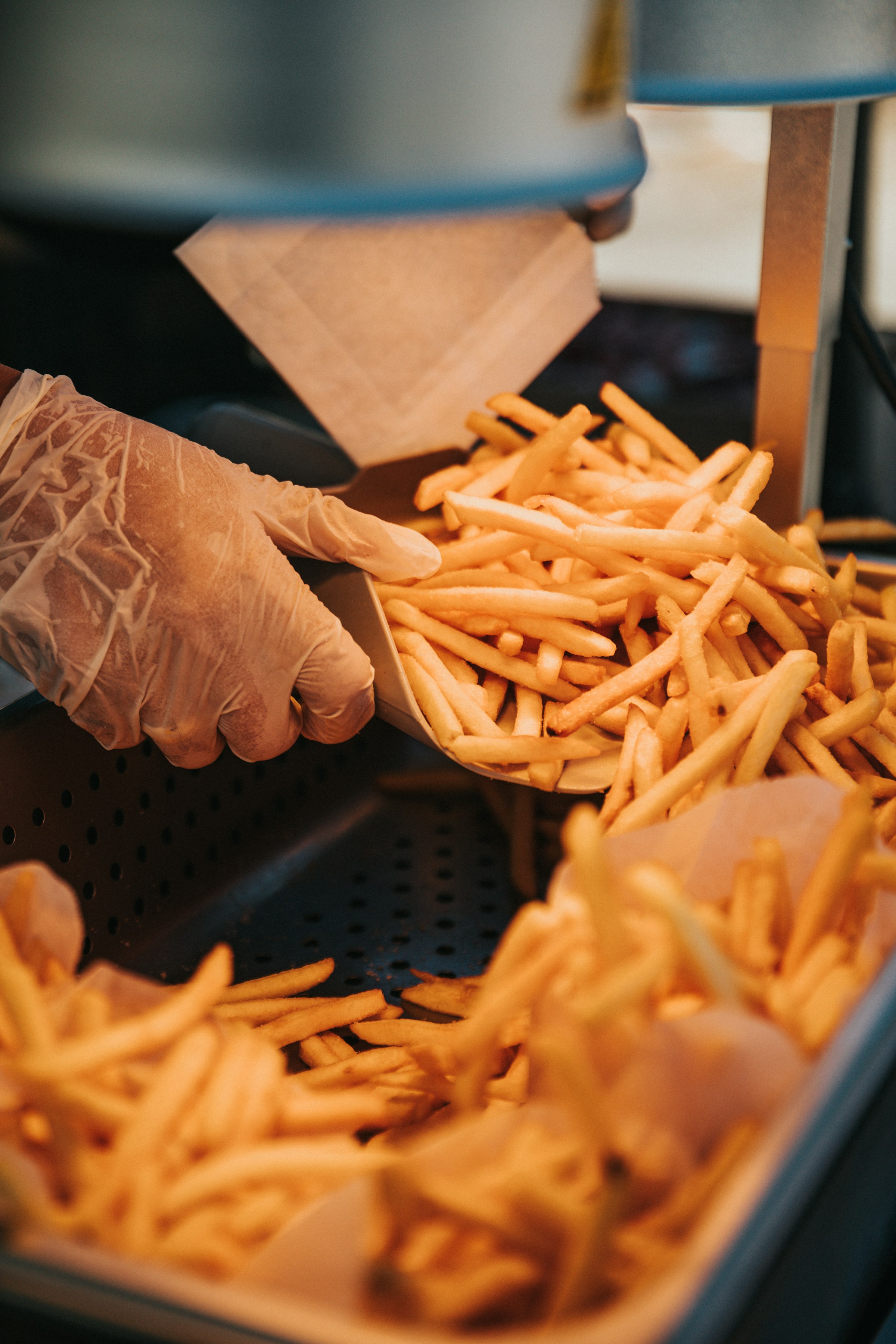 Une personne à la main gantée prélevant des frites sur une barquette | Source : Unsplash