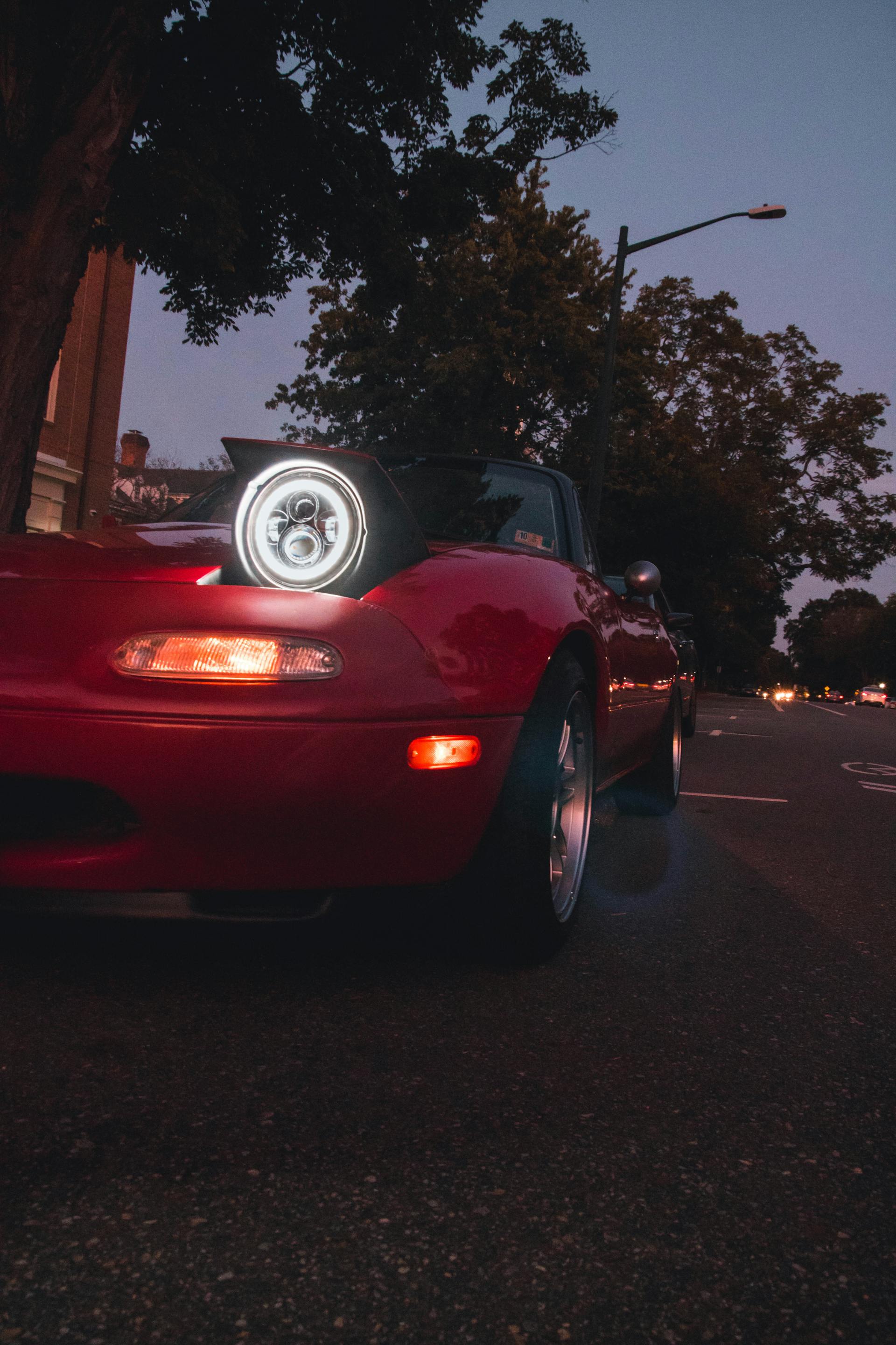 Une voiture rouge avec ses phares allumés la nuit | Source : Pexels