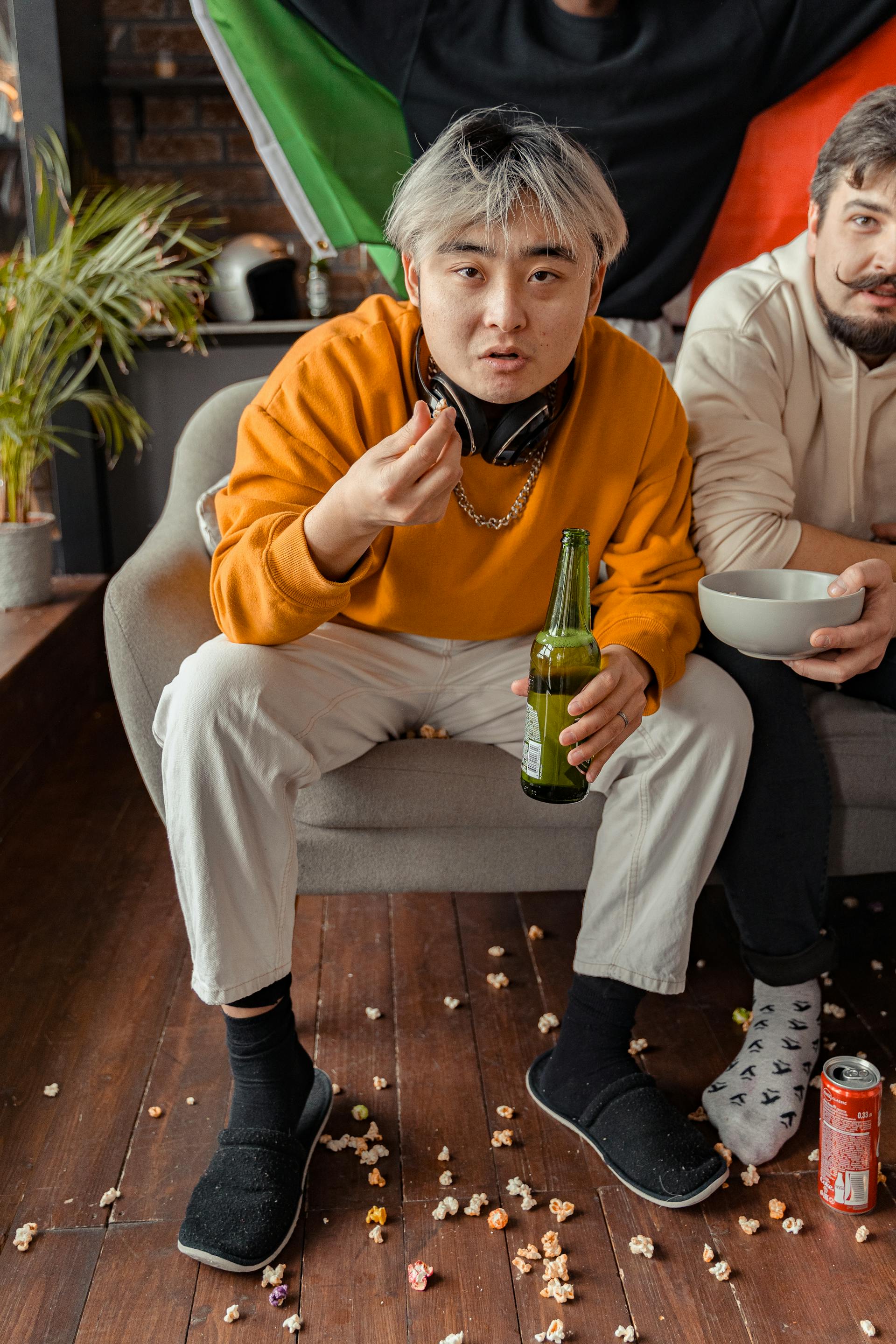 Deux hommes assis sur le canapé en train de prendre une bière et des popcorns | Source : Pexels