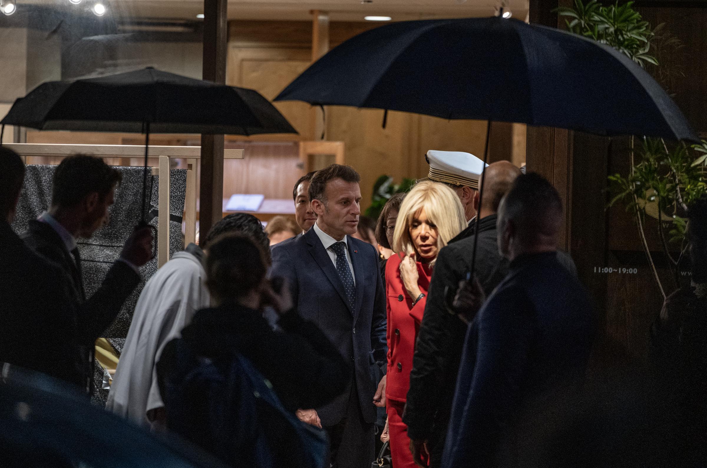 Le président français Emmanuel Macron (au centre à gauche) et son épouse Brigitte Macron (au centre à droite) quittent le showroom Ginza Motoji par une nuit pluvieuse à Tokyo, le 31 mars 2026 I Source : Getty Images