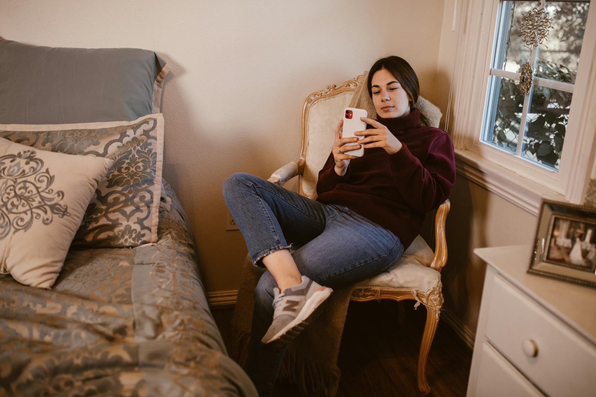 Une jeune femme assise dans un fauteuil et regardant son téléphone | Source : Pexels
