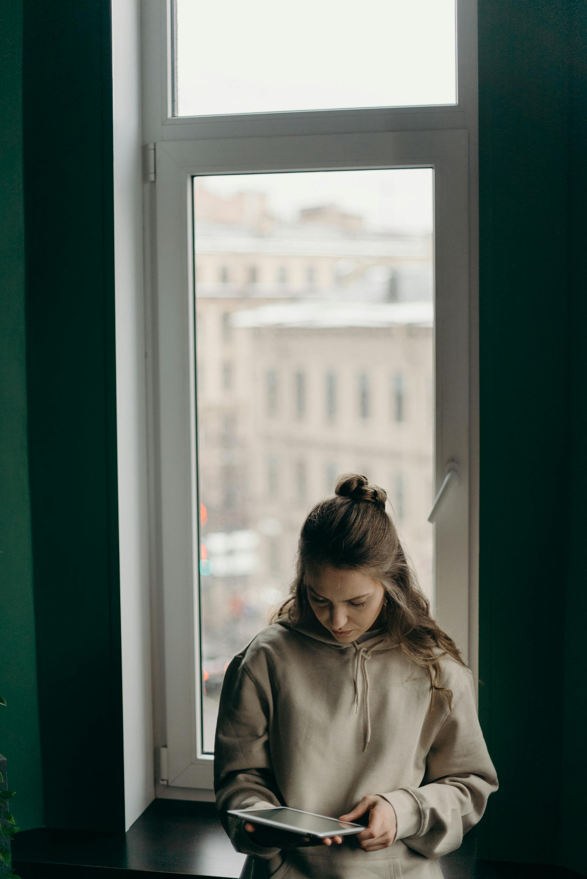 Une femme regarde son iPad en se tenant près de la fenêtre | Source : Pexels