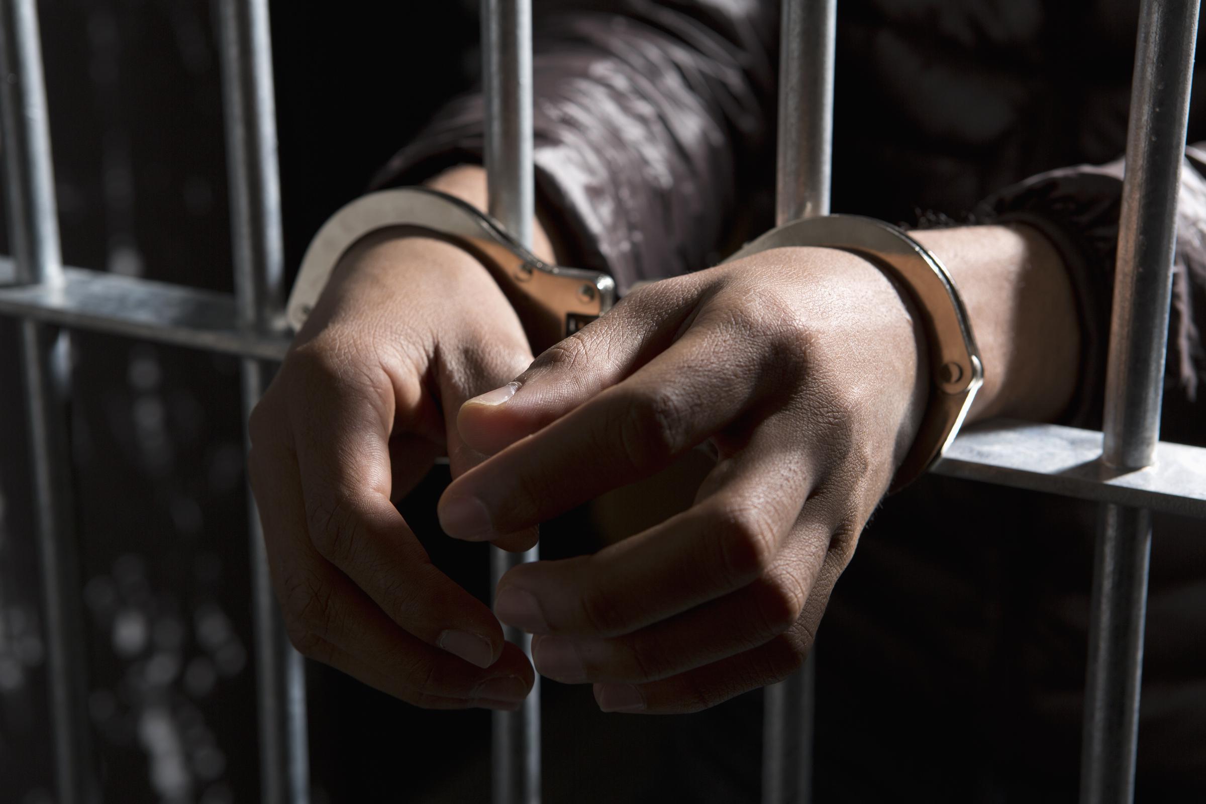 Un prisonnier derrière les barreaux, les mains menottées I Photo d'illustration I Source : Getty Images