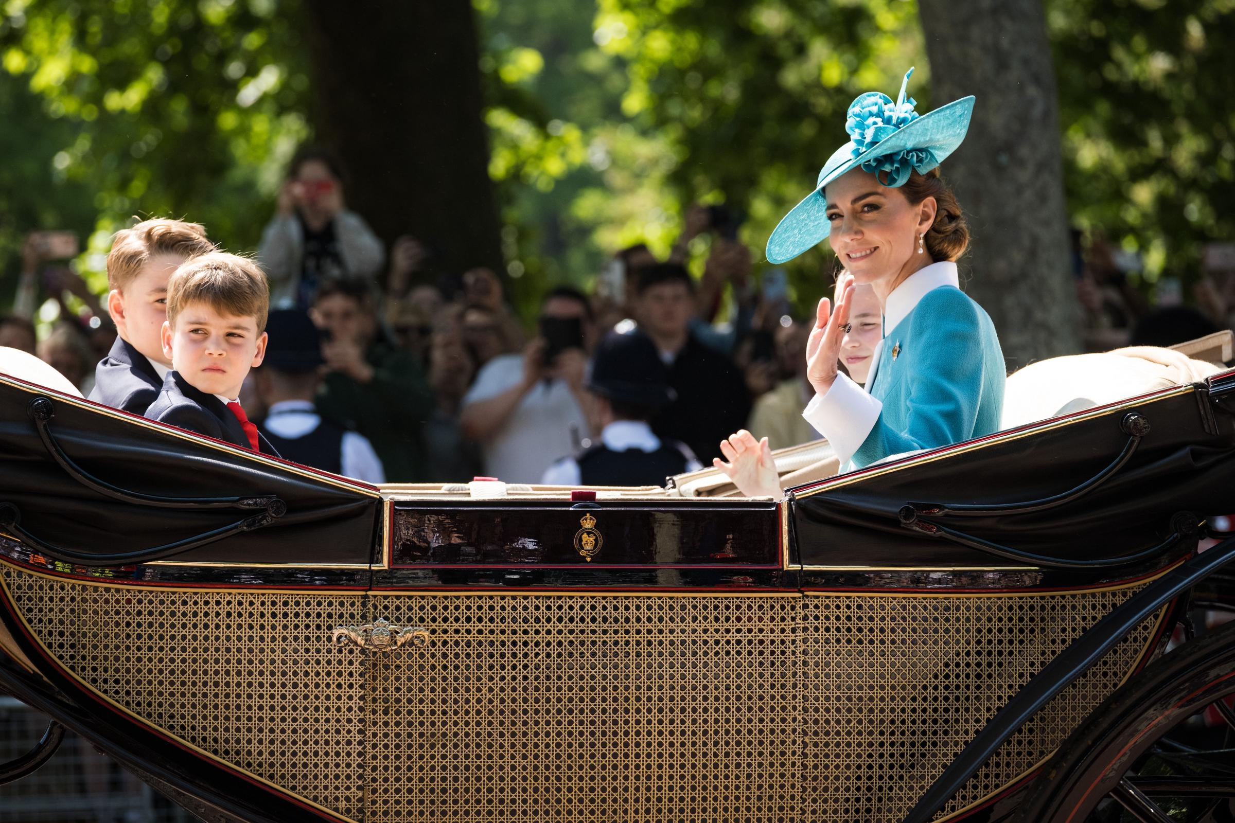La princesse Charlotte, la princesse Catherine, le prince George et le prince Louis montent dans le carrosse royal tandis que Catherine et la princesse Charlotte saluent les gens.
