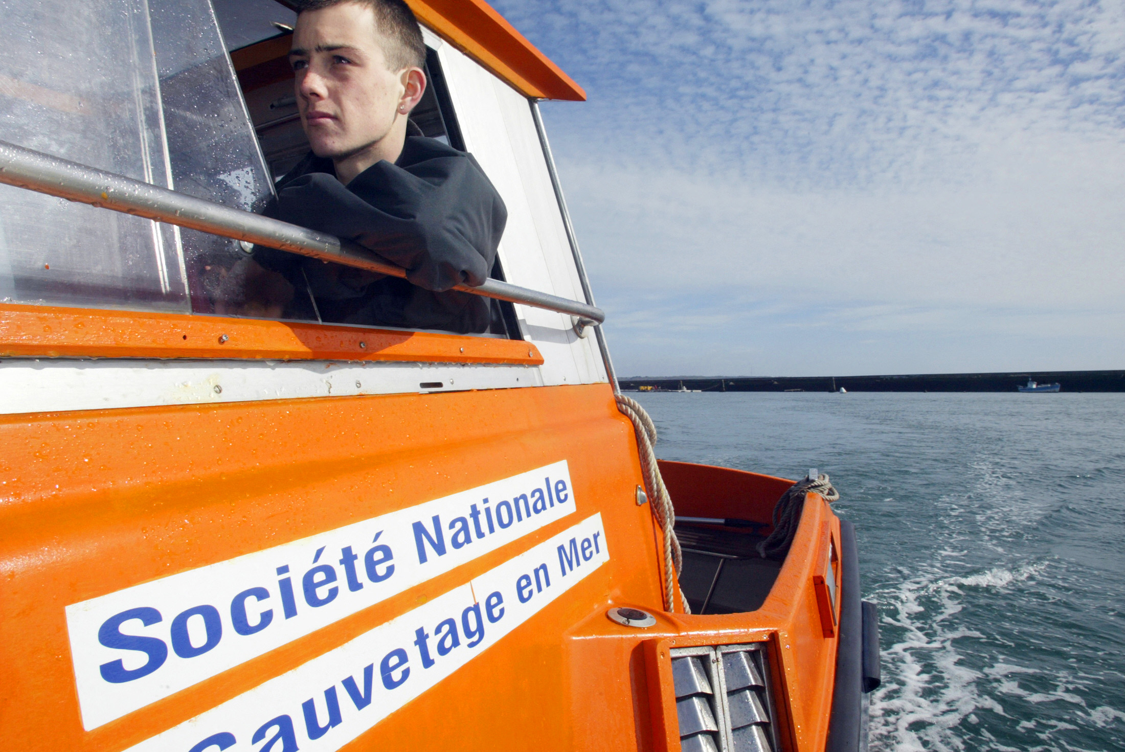 SUR SES CANOTS, LA SNSM REDONNE CONFIANCE A DES JEUNES EN DIFFICULTE ". Alexandre, un jeune en difficulté est à la barre du bateau de la SNSM (Société Nationale de Sauvetage en Mer), le 08 mars 2007 dans la rade de Brest (Finistère), dans le cadre d'un projet destiné à favoriser son insertion I Photo d'illustration I Source : Getty Images
