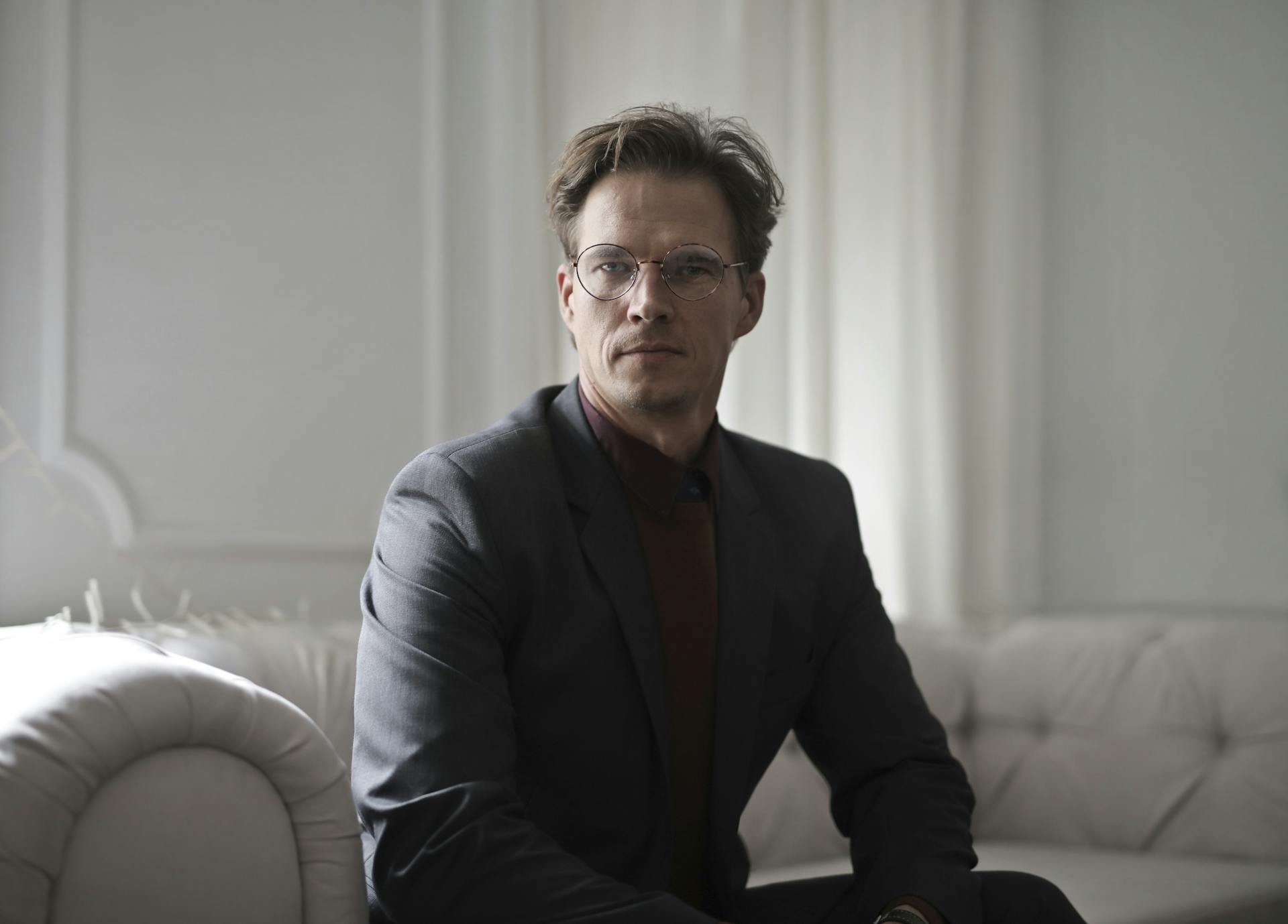 Un homme portant un blazer et des lunettes assis sur un canapé | Source : Pexels
