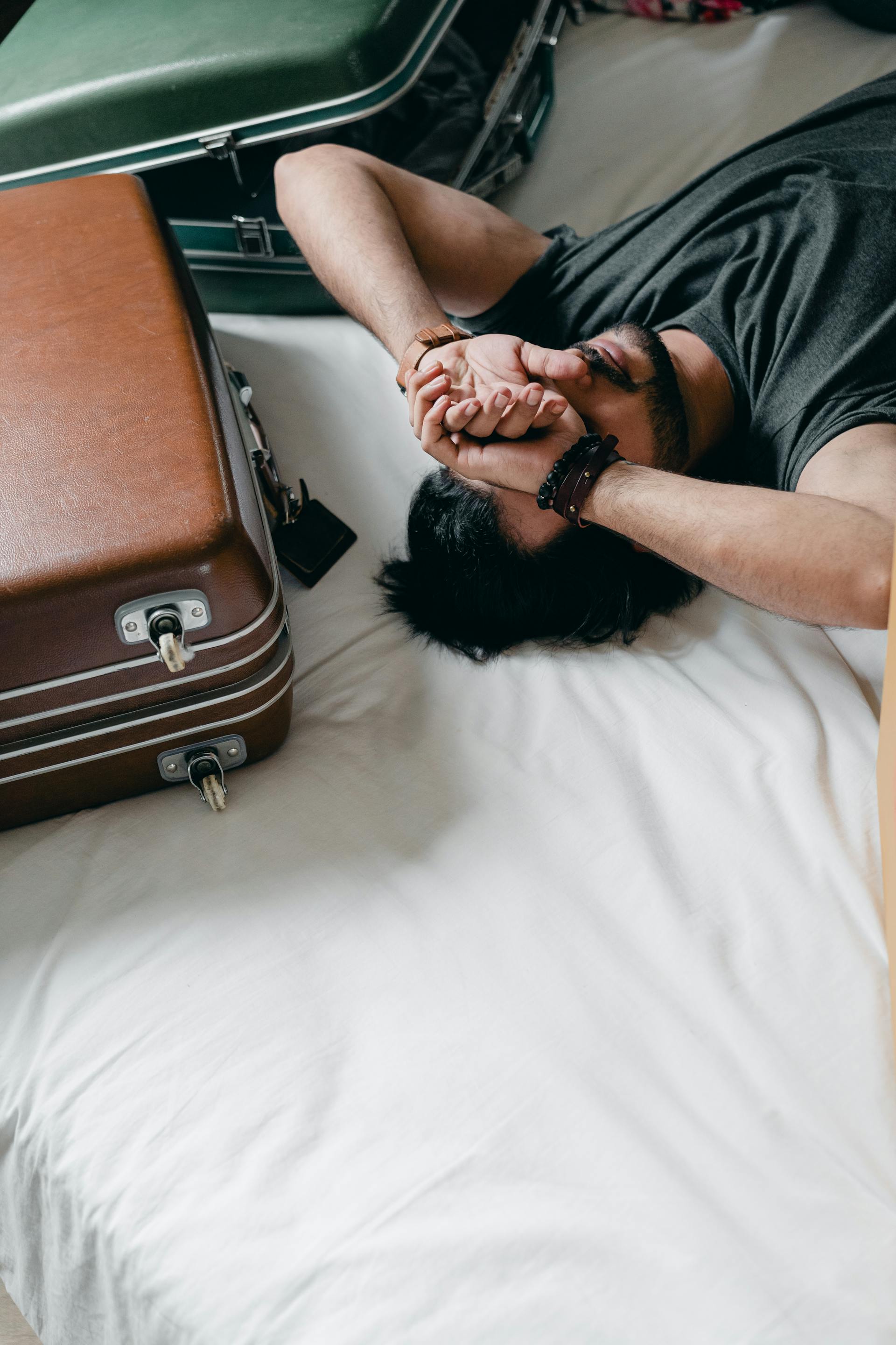 Un homme fatigué allongé sur un lit à côté de valises | Source : Pexels