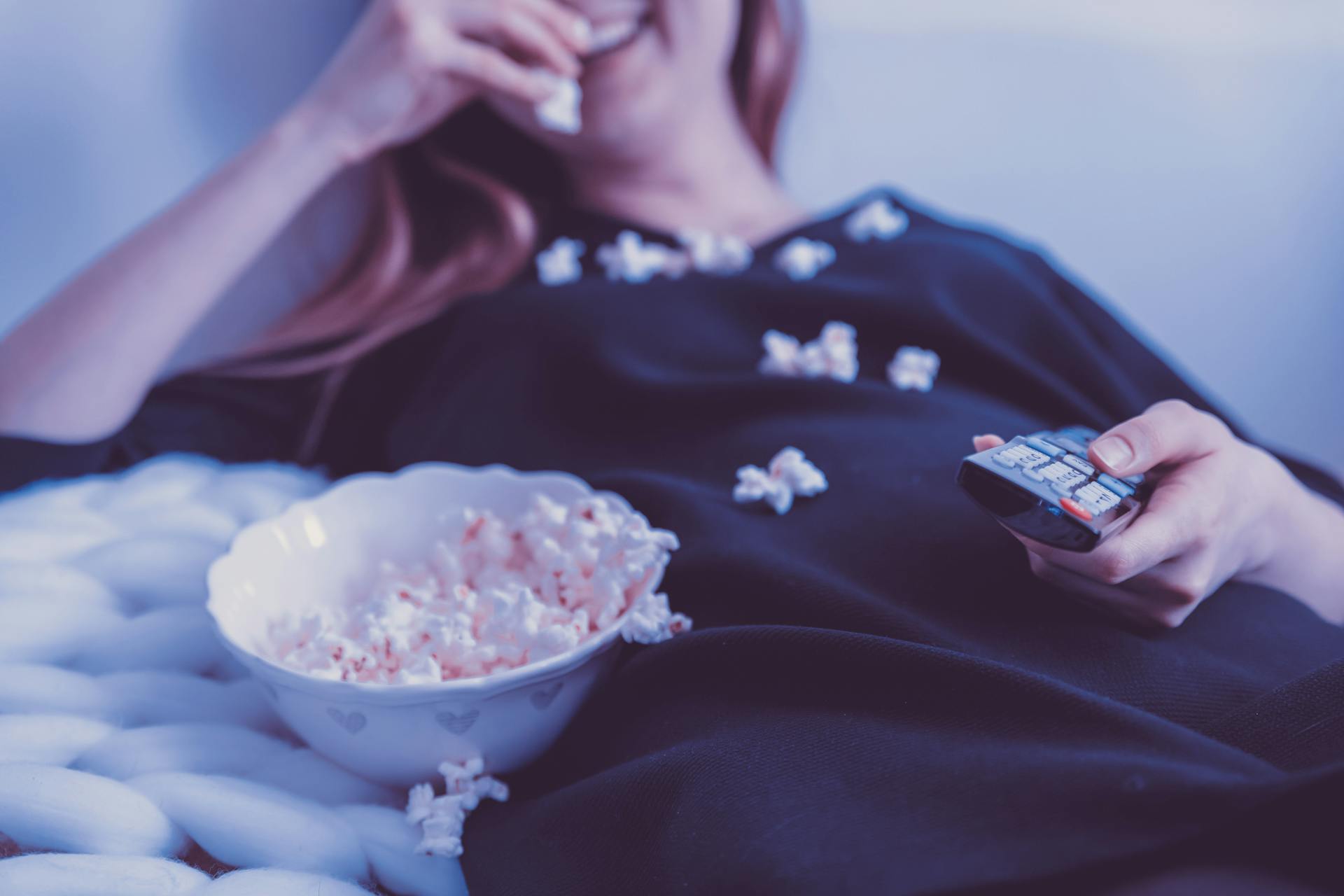 Une femme mange du pop-corn tout en tenant une télécommande de télévision | Source : Pexels