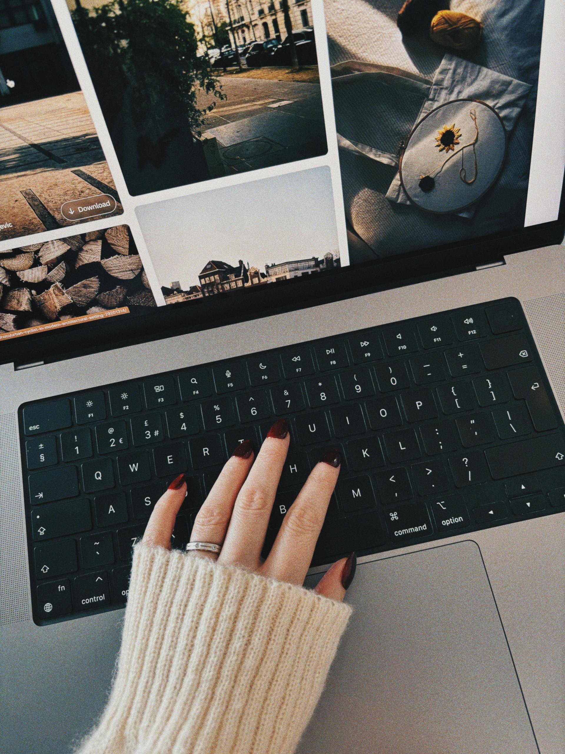 Une personne avec des ongles manucurés en rouge et un pull blanc utilisant son ordinateur portable | Source : Pexels