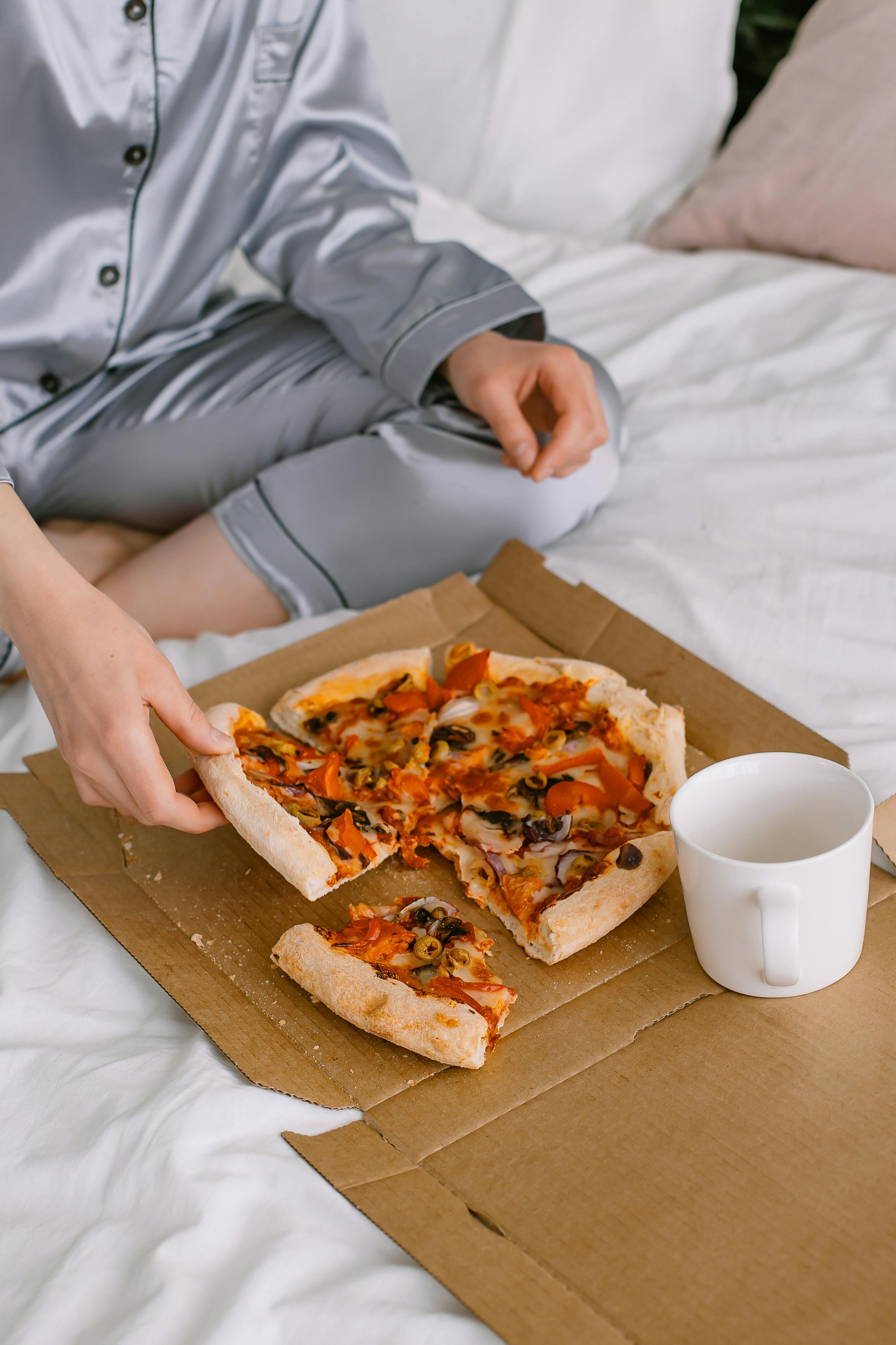 Une personne assise sur un lit avec une boîte de pizza | Source : Pexels