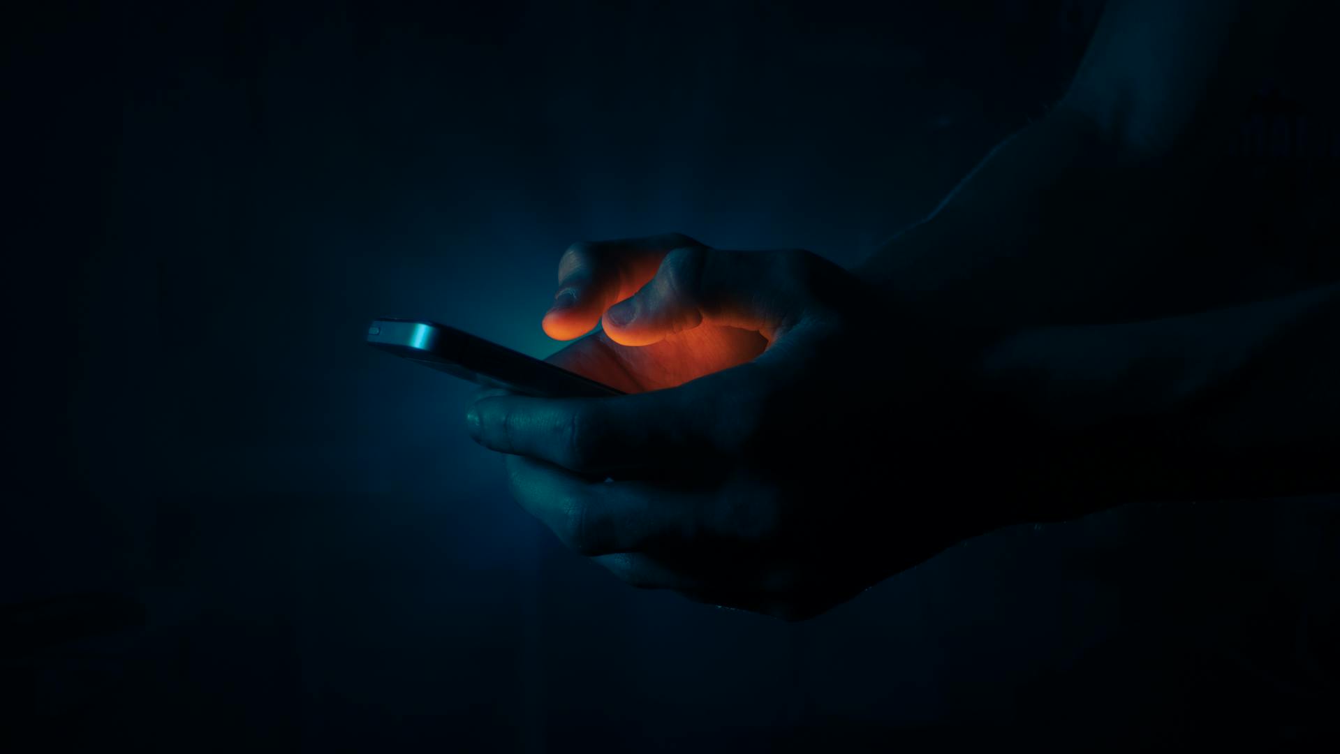 Un homme tenant un téléphone dans l'obscurité | Source : Pexels