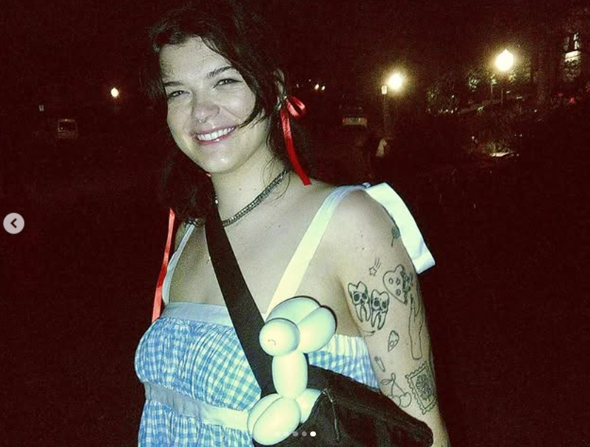 Kendall Fortner sourit, vêtue d'une robe vichy bleue avec des rubans rouges dans les cheveux et un animal ballon ludique accroché à son sac | Source : Instagram/kendall_fortner