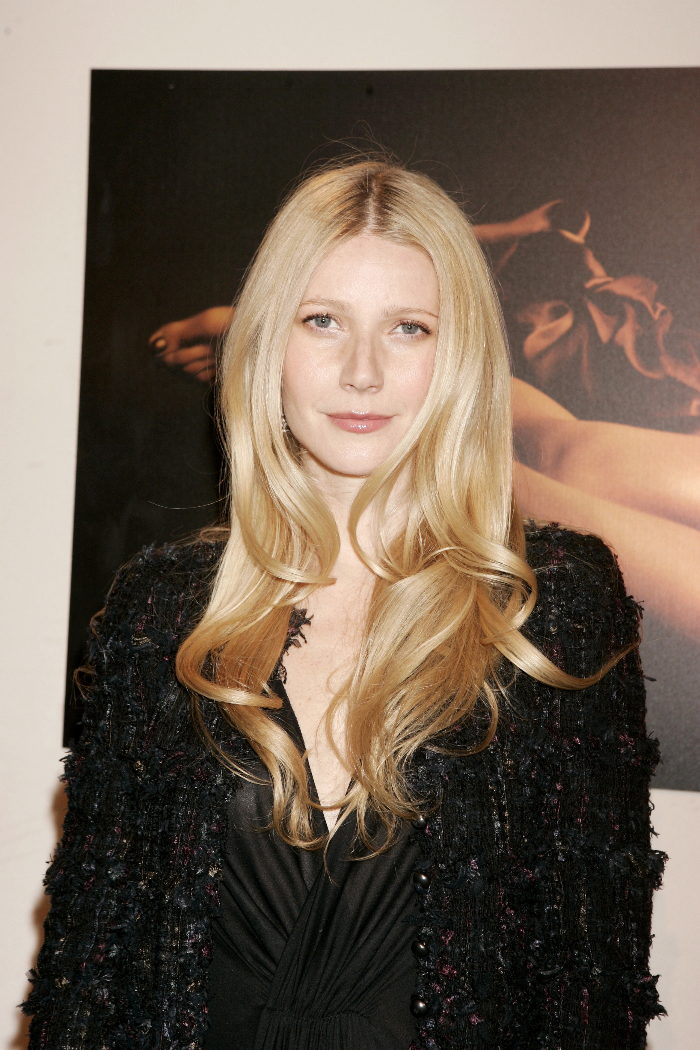 Gwyneth Paltrow assiste à l'événement Tom Ford Estée Lauder Collection en 2005, vêtue d'une veste noire texturée superposée à une robe à décolleté en V profond. Ses longs cheveux blonds sont coiffés en boucles souples et volumineuses avec une raie au milieu, tandis que son maquillage naturel, rehaussé d'un gloss rose pâle, lui donne un air lumineux et élégant.