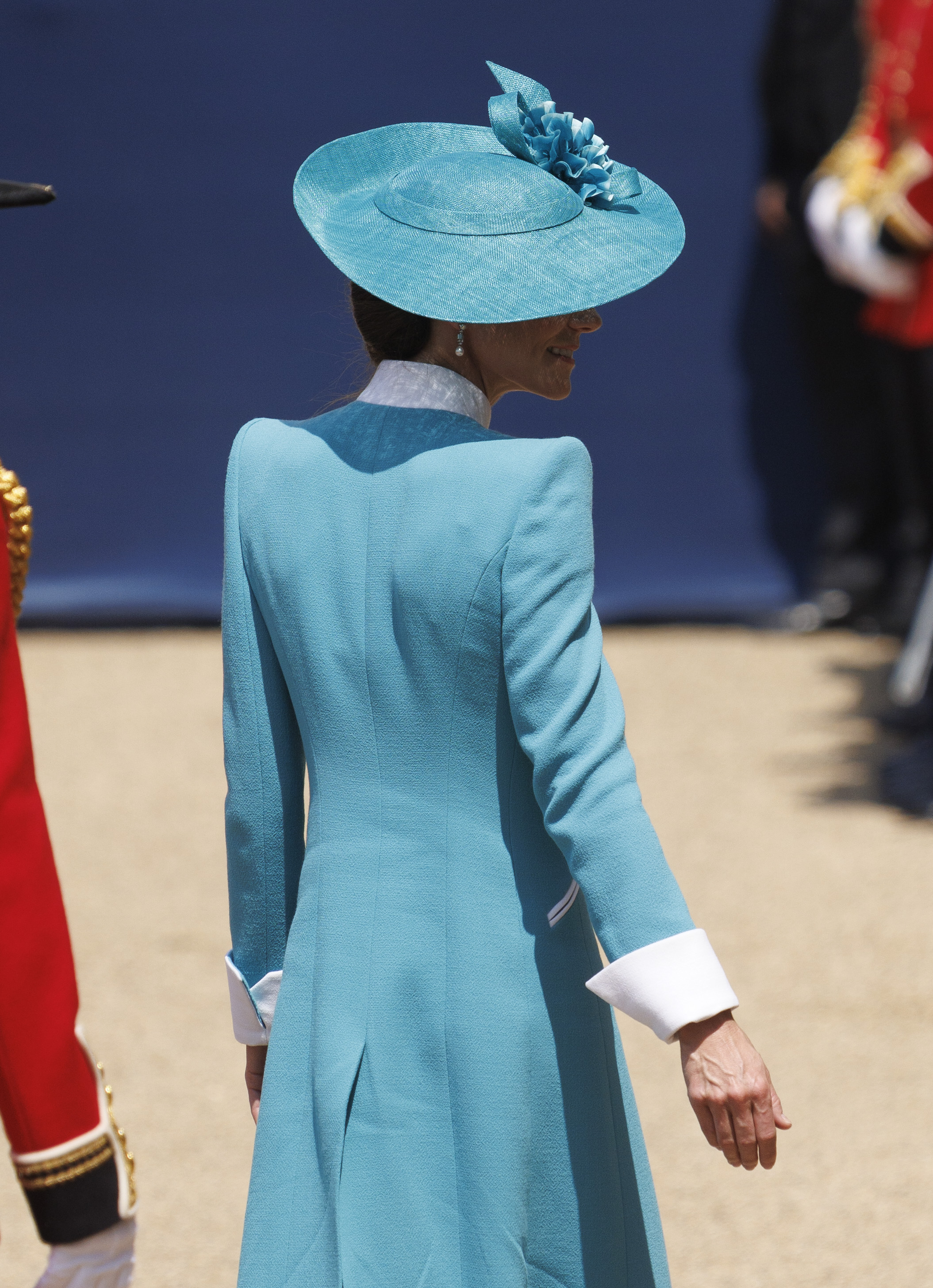 Sur une photo prise de dos lors de la parade Trooping the Colour de 2025, on aperçoit la princesse Catherine vêtue d'un magnifique manteau bleu sarcelle rehaussé de touches de blanc éclatant, alors qu'elle assiste à la parade cérémonielle. Son chapeau assorti et son élégante coiffure relevée complètent son look, lui conférant une silhouette gracieuse qui reflète à la fois la tradition et le style royal moderne.