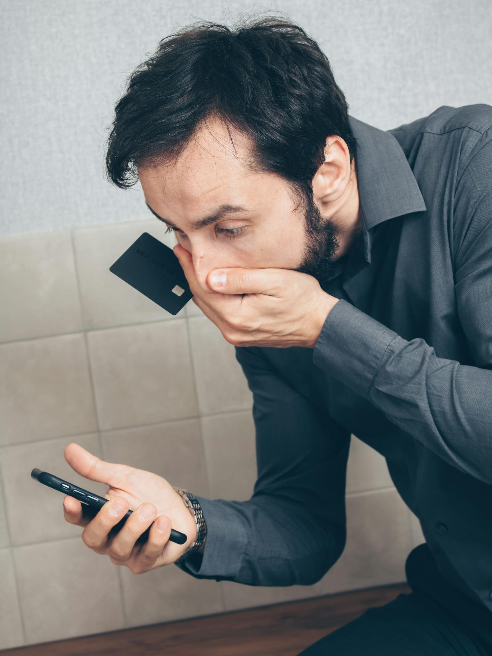 Un homme tenant une carte de crédit fixe son téléphone en état de choc | Source : Pexels