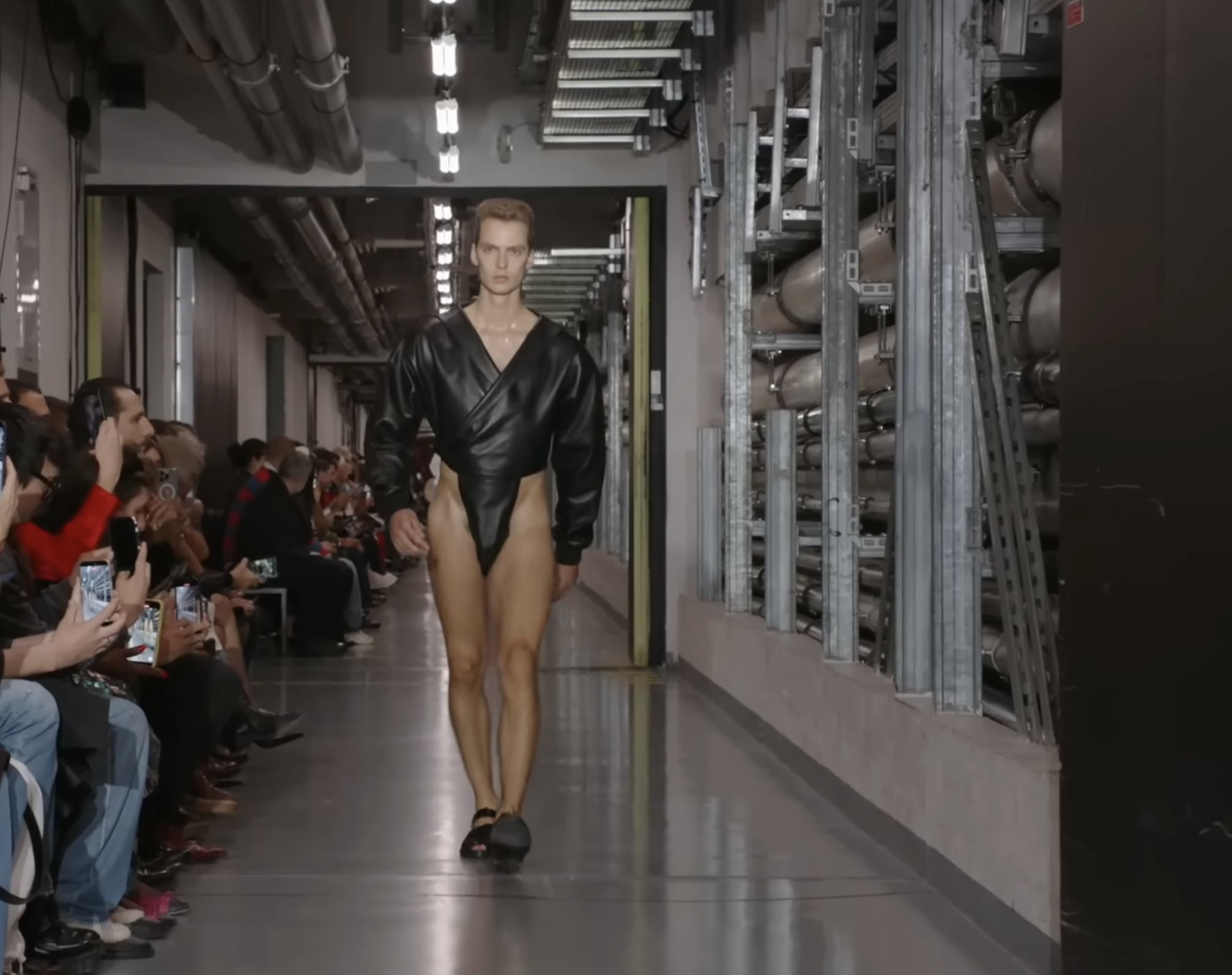 Ce mannequin porte une version noire au design volumineux et gonflé qui met en valeur ses jambes musclées — une interprétation distinctive du body, adaptée à la morphologie masculine. Extrait d'une publication datée du 5 octobre 2025. Source : Youtube/@jeanpaulgaultier