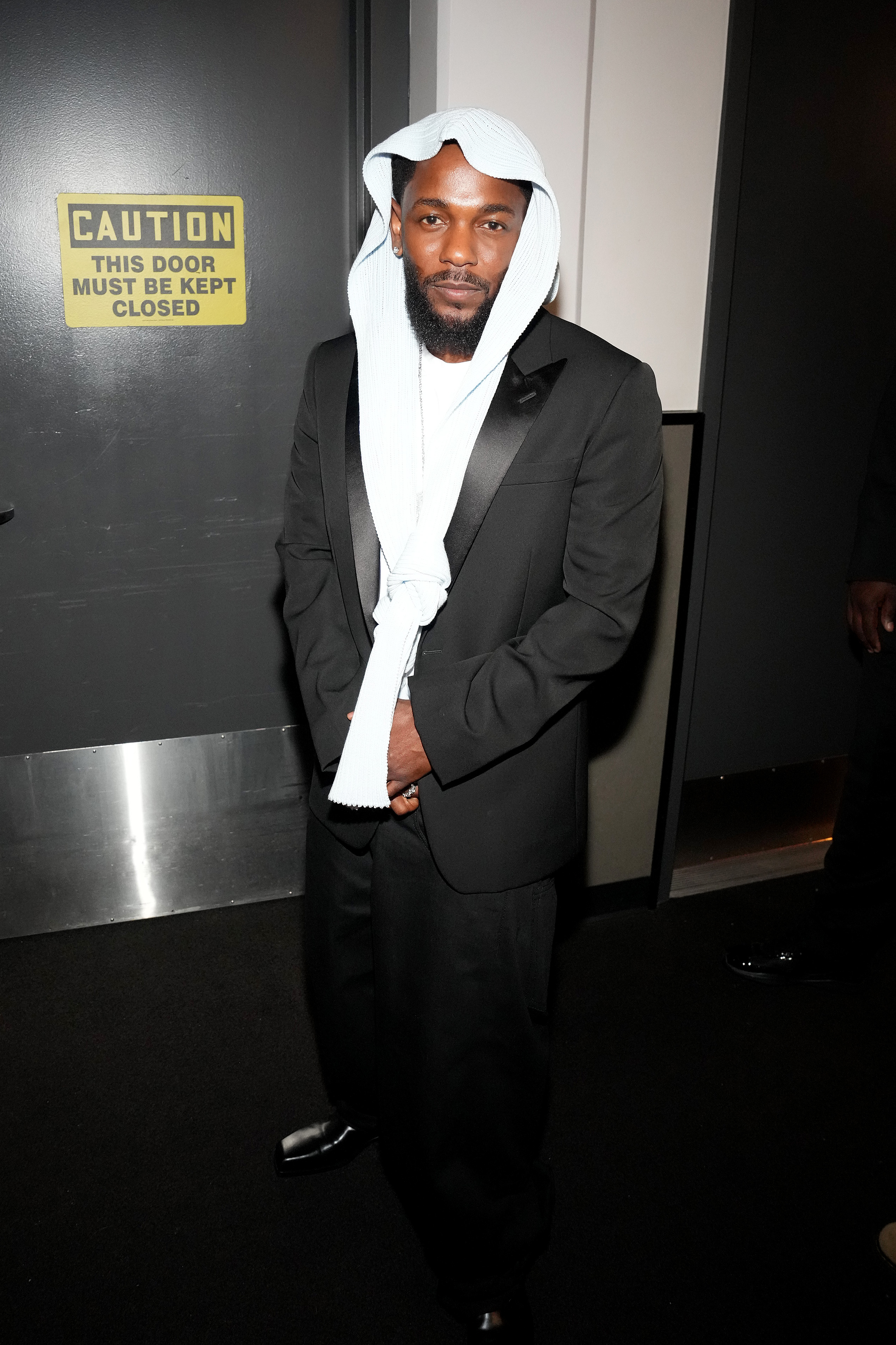 Dans les coulisses du Peacock Theater, Kendrick Lamar pose dans son look complet des BET Awards 2025 - un smoking noir associé au couvre-chef désormais iconique, noué sur le devant, qui a suscité curiosité et commentaires sur les réseaux sociaux.