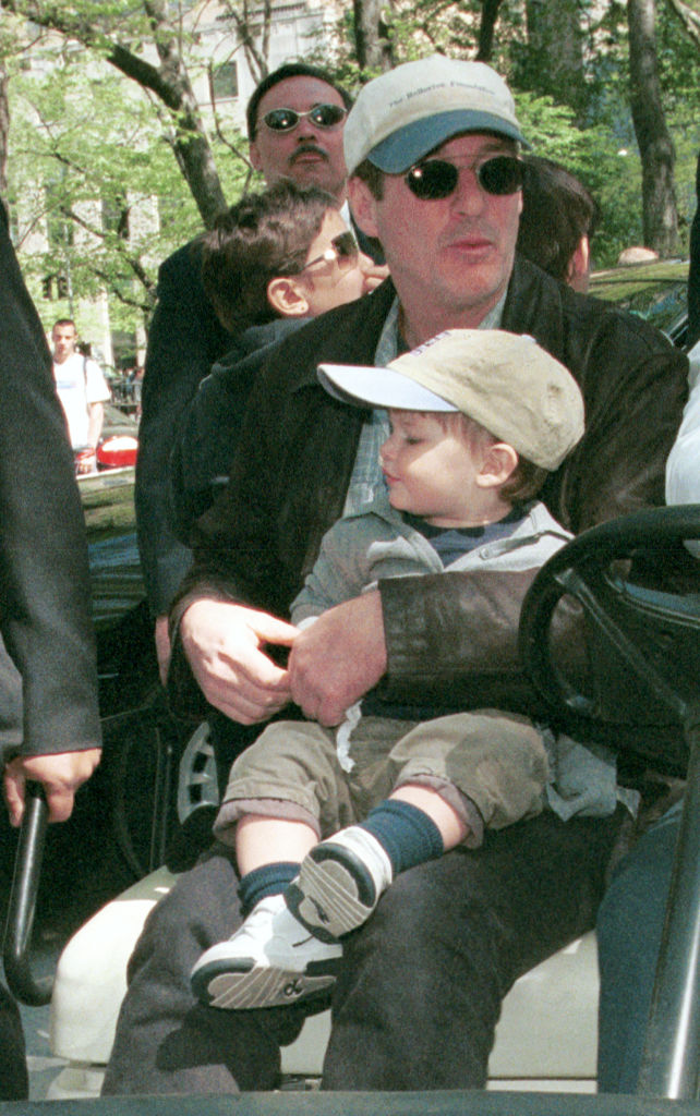 Portant des casquettes assorties, Richard Gere et son fils Homer Gere sont présents au carnaval « Kids for Kids » à Central Park, New York. Assis ensemble, ils profitent tranquillement de l'événement qui se déroule autour d'eux (2001)