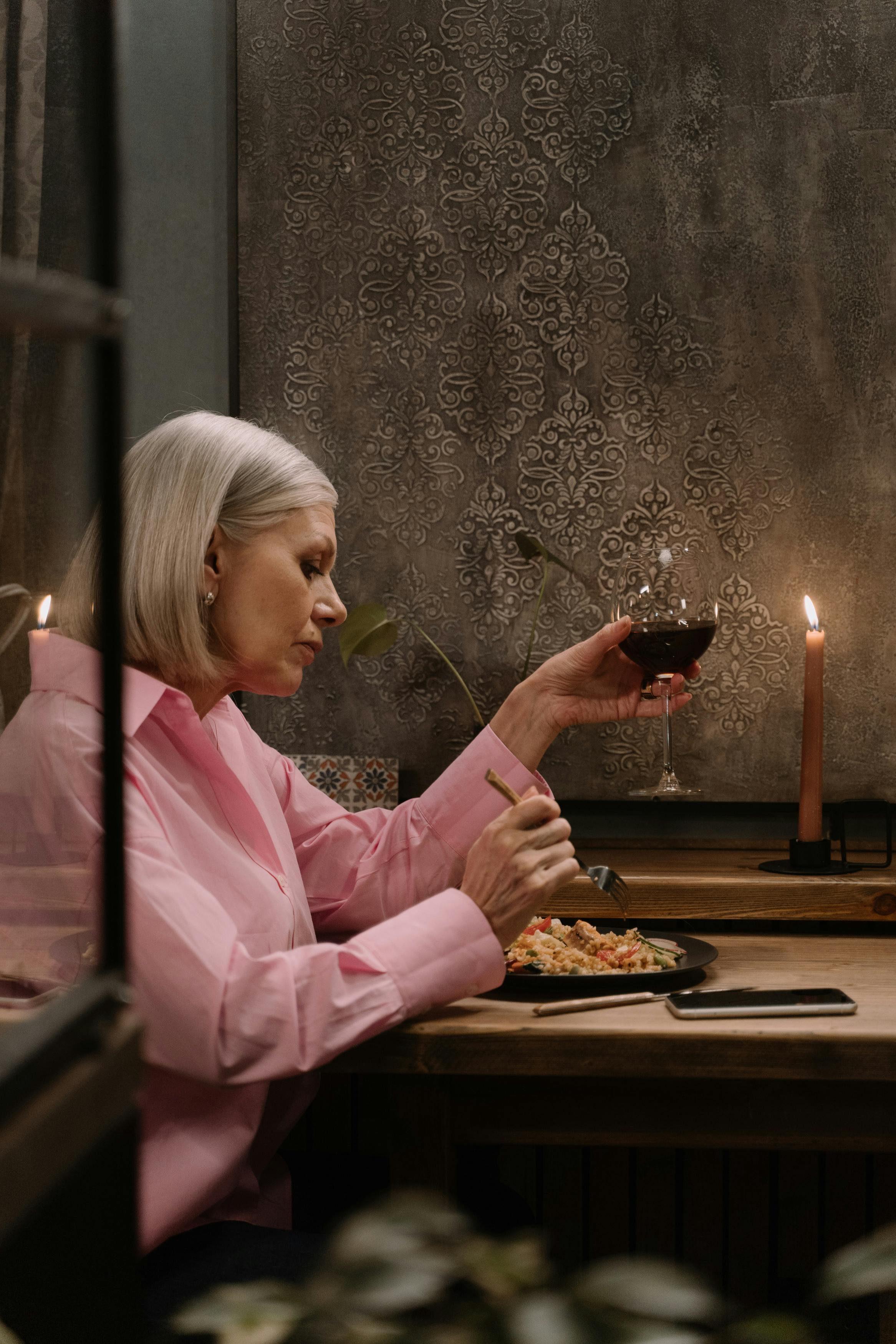 Femme tenant un verre de vin tout en mangeant | Source : Pexels