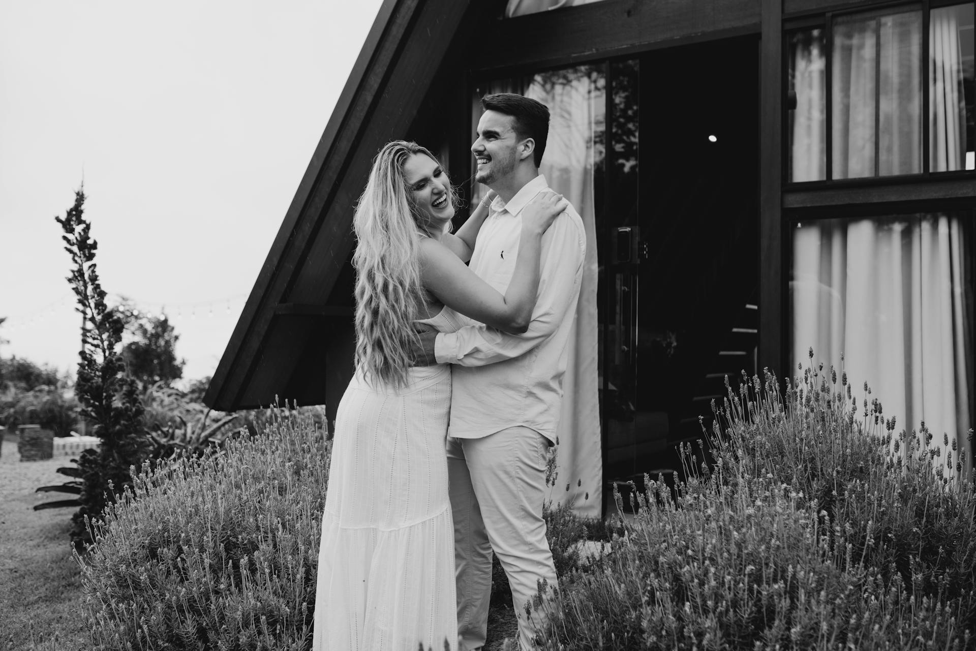 Un couple souriant, s'étreint devant une cabane moderne à ossature en A | Source : Pexels