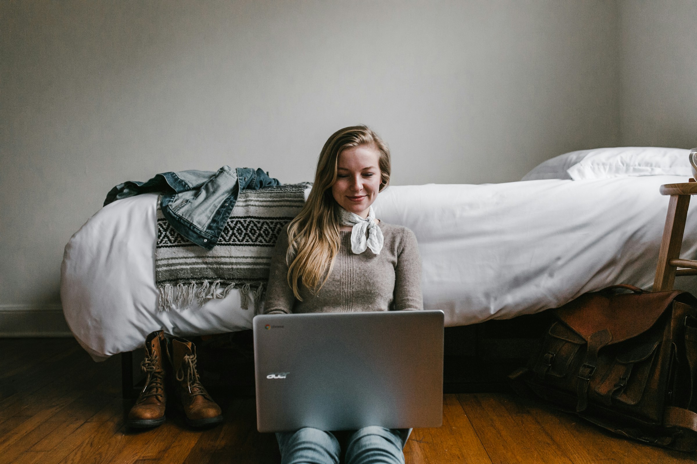 Une femme assise à côté de son lit tout en utilisant un ordinateur portable | Source : Unsplash