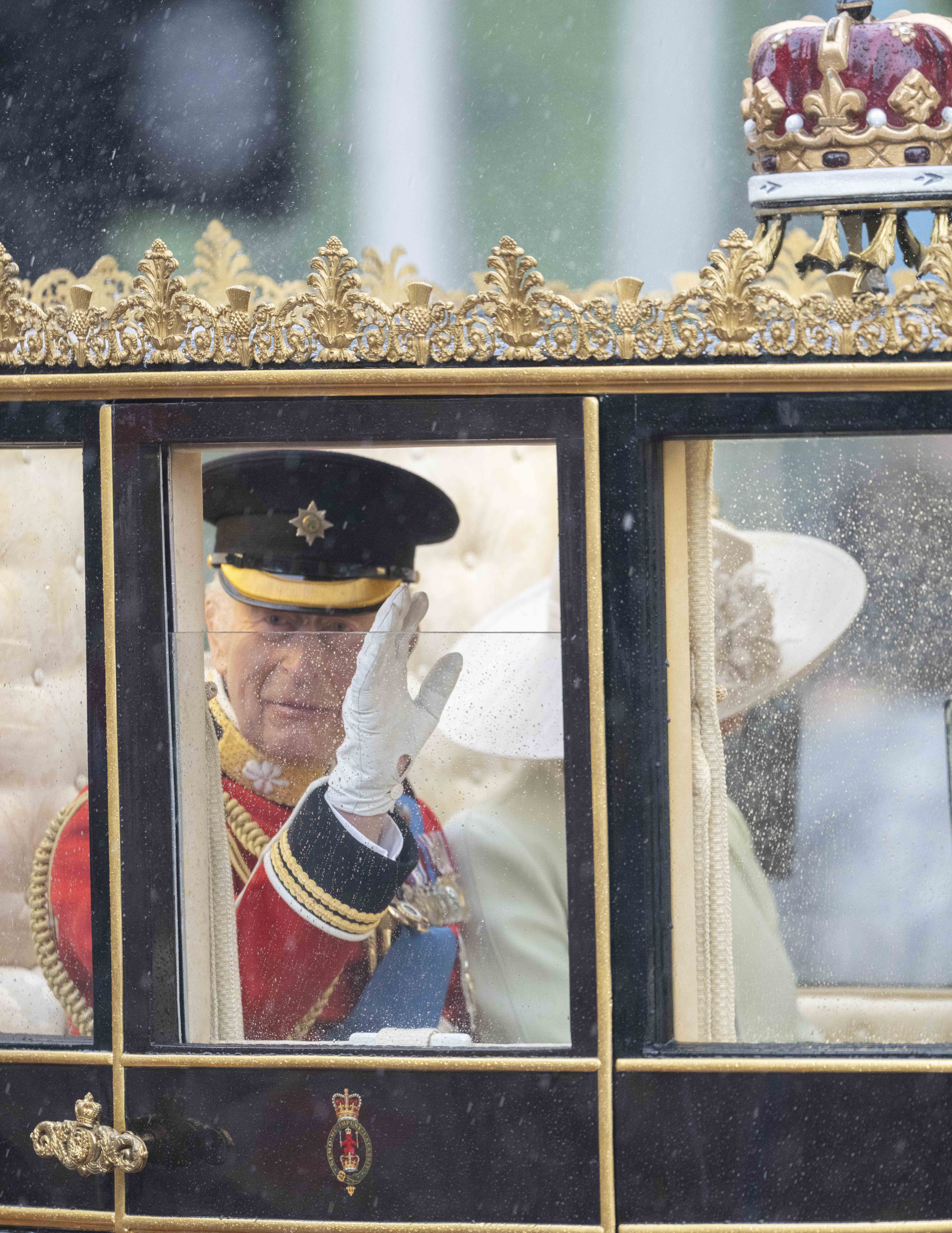 À travers une vitre éclaboussée par la pluie, le roi Charles III reconnaît les spectateurs lors de la procession du Trooping the Colour le 15 juin 2024 | Source : Getty Images