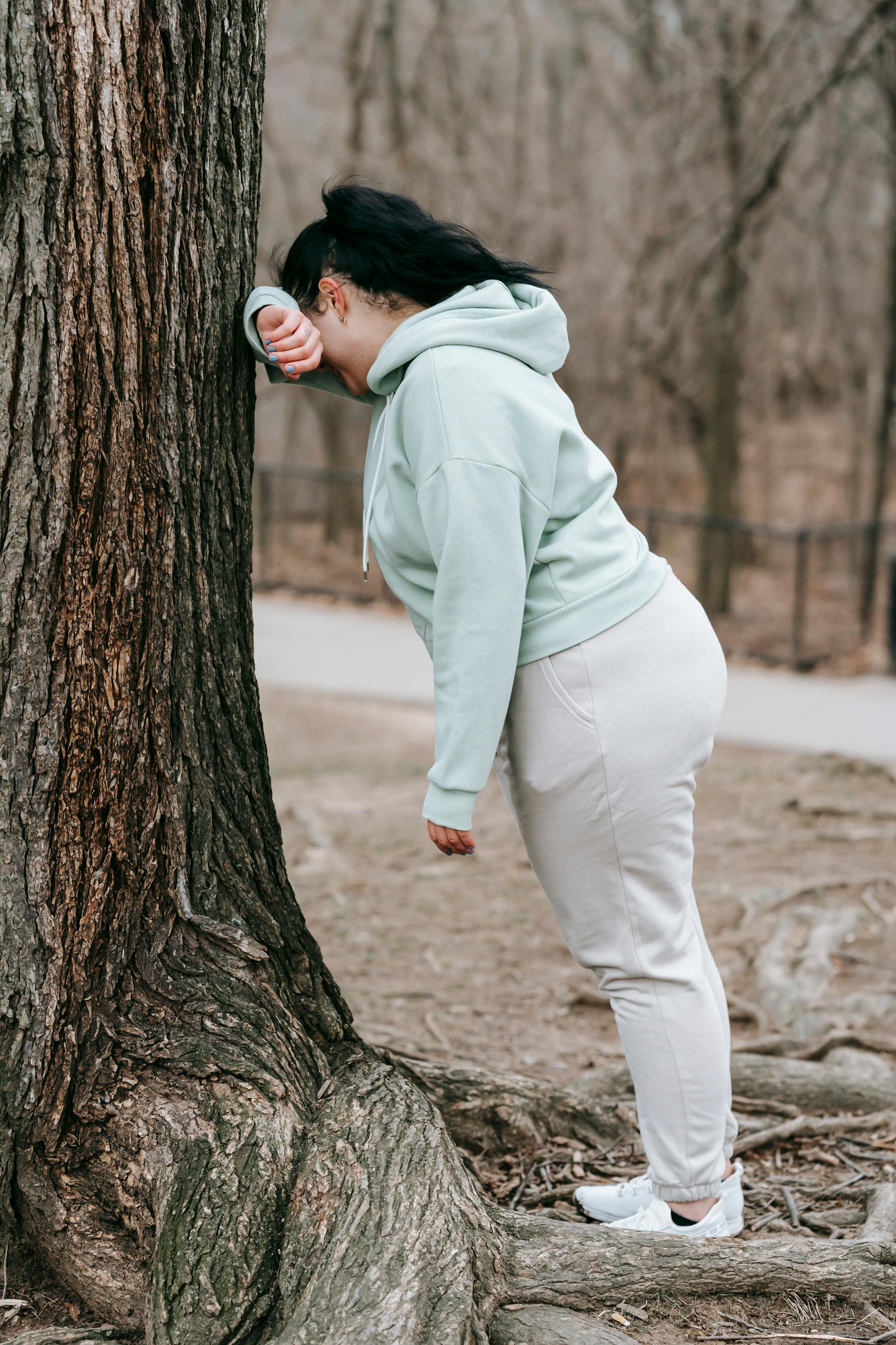 Une femme en tenue de sport appuyée sur un arbre dans un parc | Source : Pexels