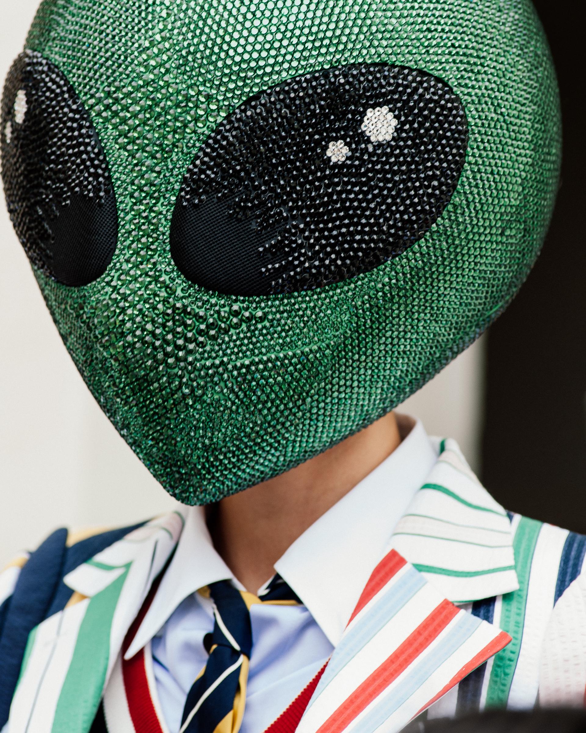 Un gros plan capture la grande tête verte de l'extraterrestre aux yeux noirs, évoquant une scène tout droit sortie d'un film d'extraterrestres de Marvel. Ce look rompt avec les normes habituelles de la Fashion Week de Paris, introduisant une touche cinématographique audacieuse sur le podium.