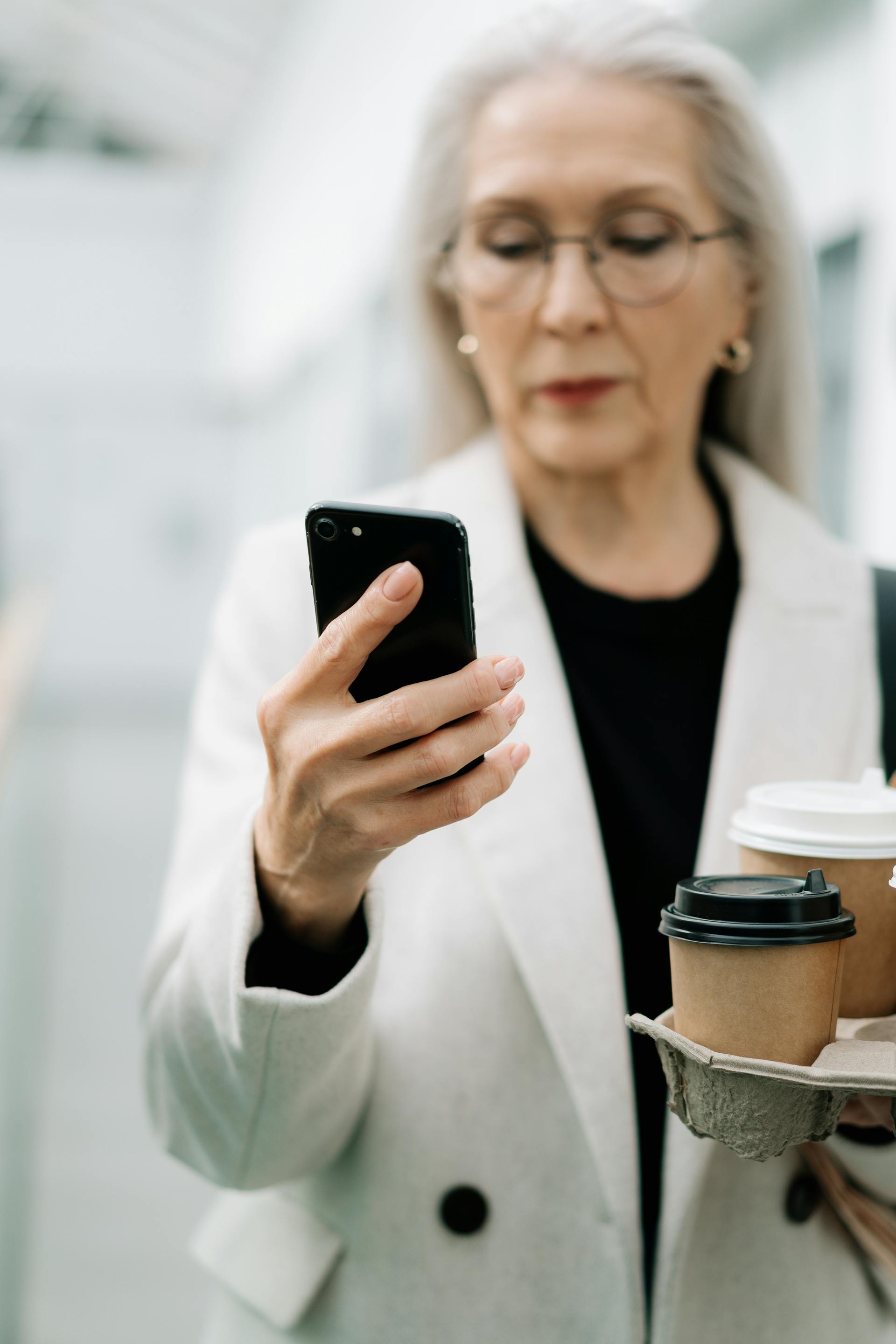 Une femme âgée utilisant son téléphone tout en tenant un café | Source : Pexels