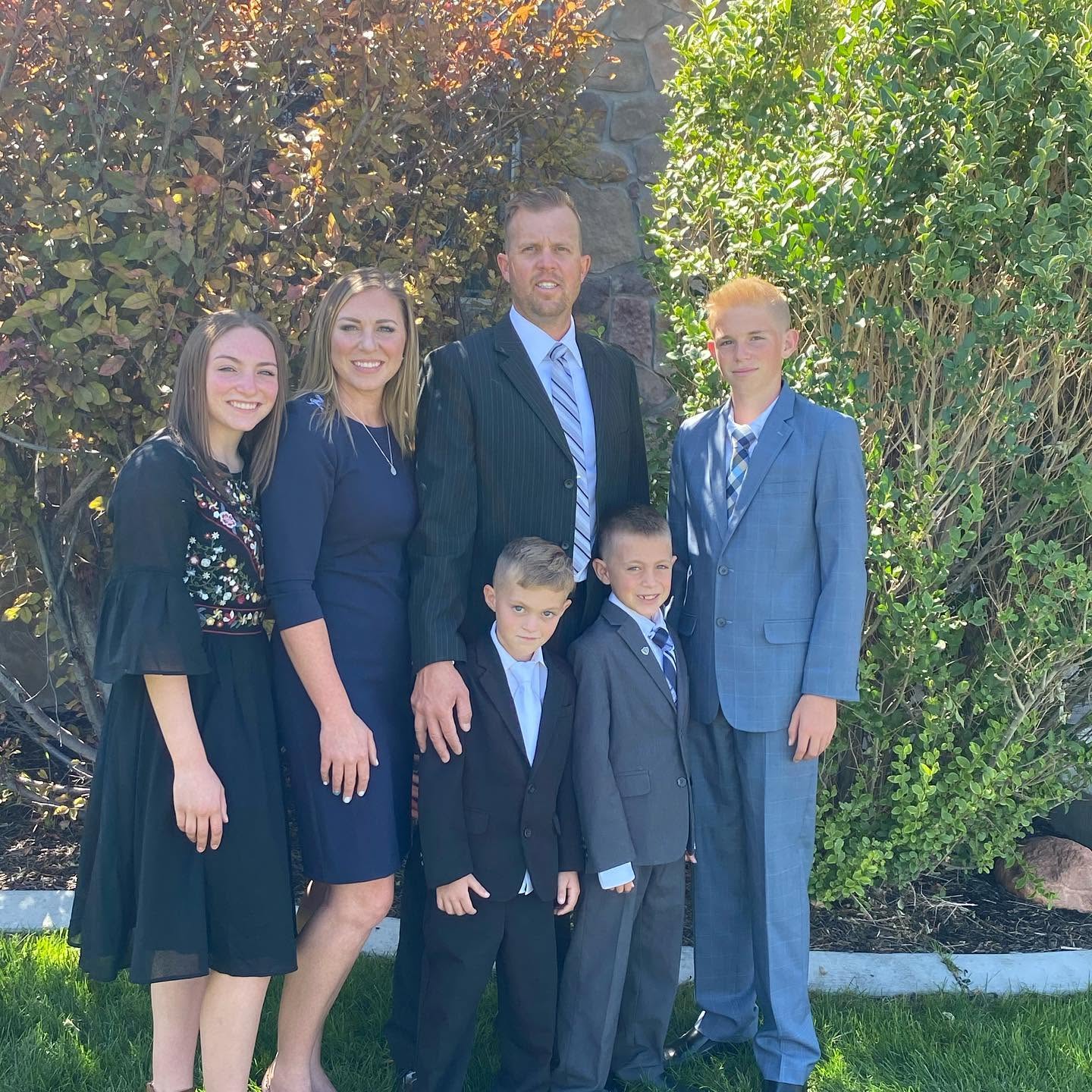 Toute la famille Long pose en photo officielle en extérieur, avec en arrière-plan un feuillage verdoyant et un mur de pierre. Katrina est super élégante dans sa tenue bleu marine, Lydia porte une robe noire aux détails raffinés, et le capitaine Spencer a fière allure aux côtés de ses trois fils, Reid, Thayne et Gage, tous vêtus de leurs plus beaux costumes. | Source : Facebook/katrina.g.long
