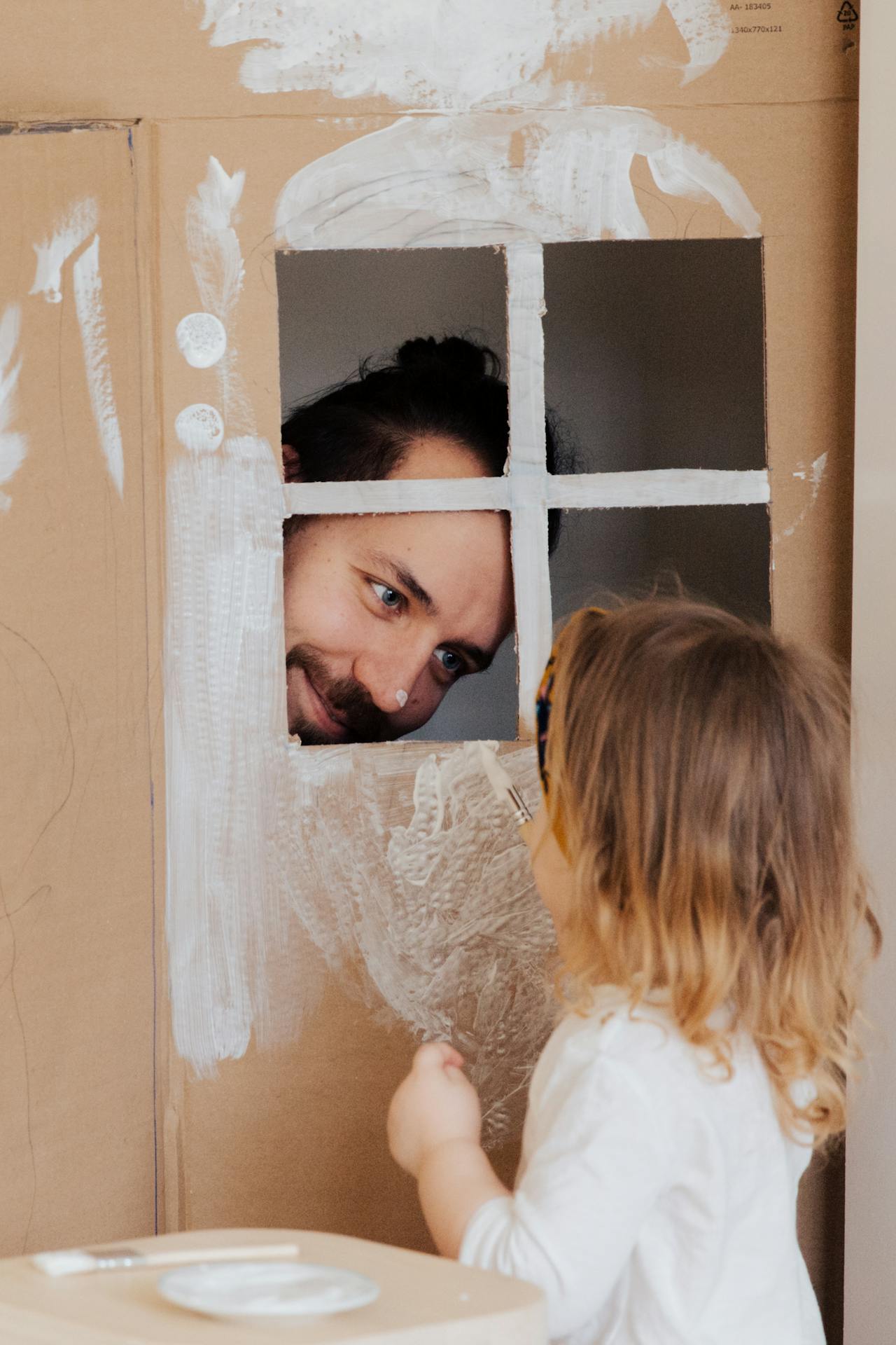 Un homme jouant avec sa petite fille pendant qu'elle peint sa maison-jouet | Source : Pexels