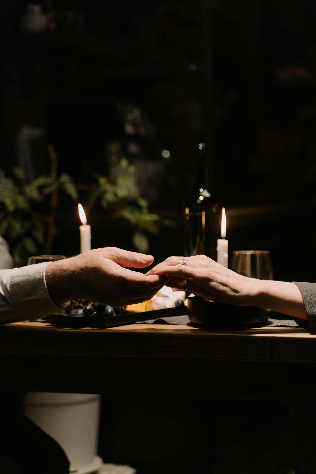 Gros plan sur un couple se tenant par la main sur fond de dîner aux chandelles | Source : Pexels