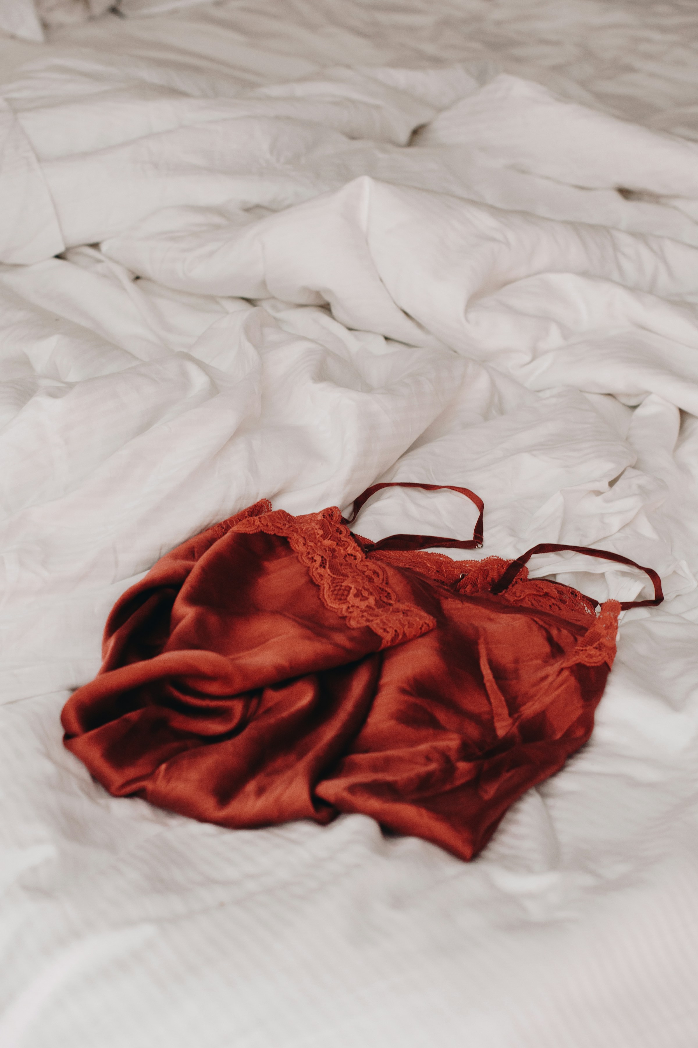 Lingerie rouge lacée posée sur des draps blancs en lin | Source : Unsplash
