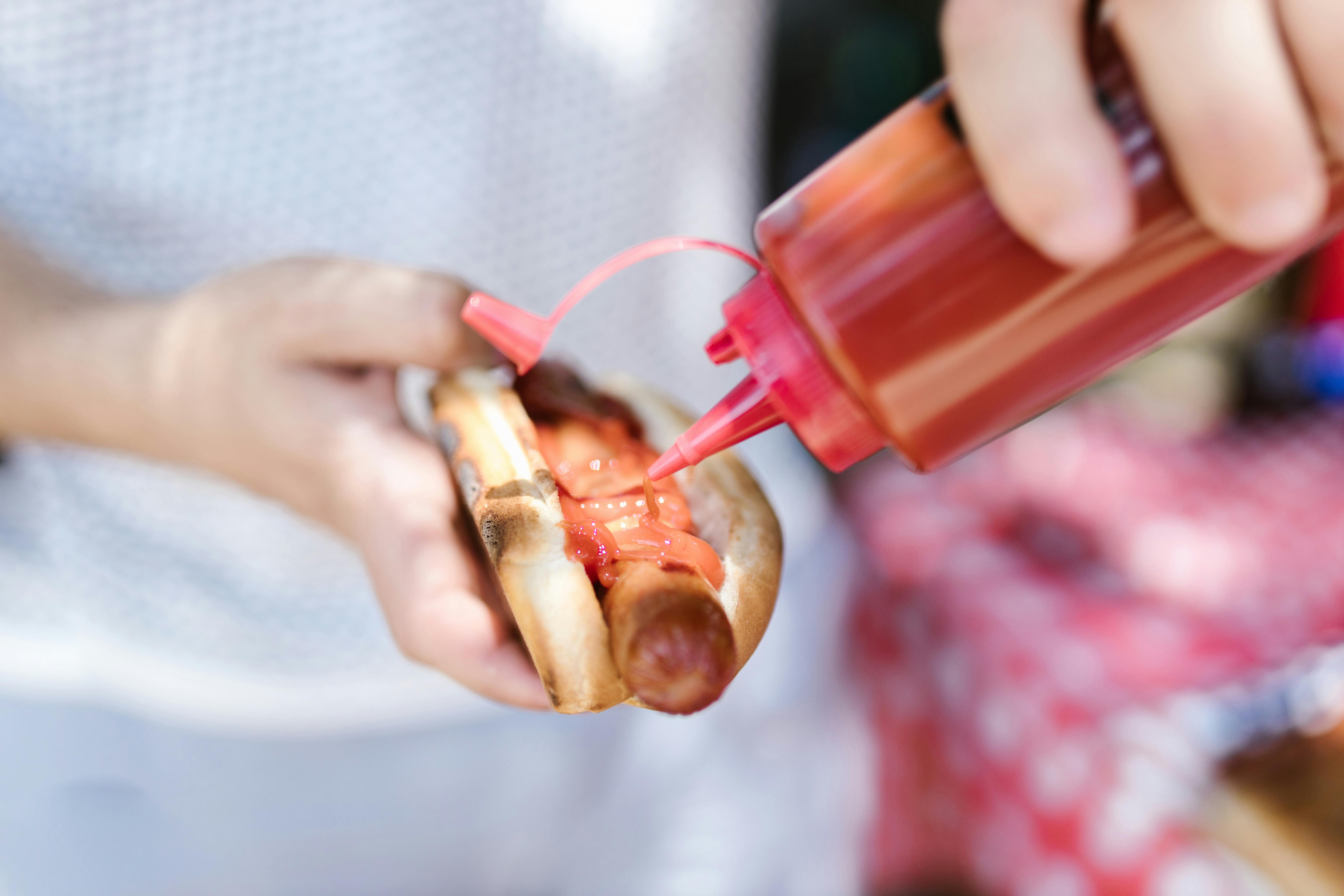 Une personne mettant du ketchup sur un hotdog | Source : Pexels
